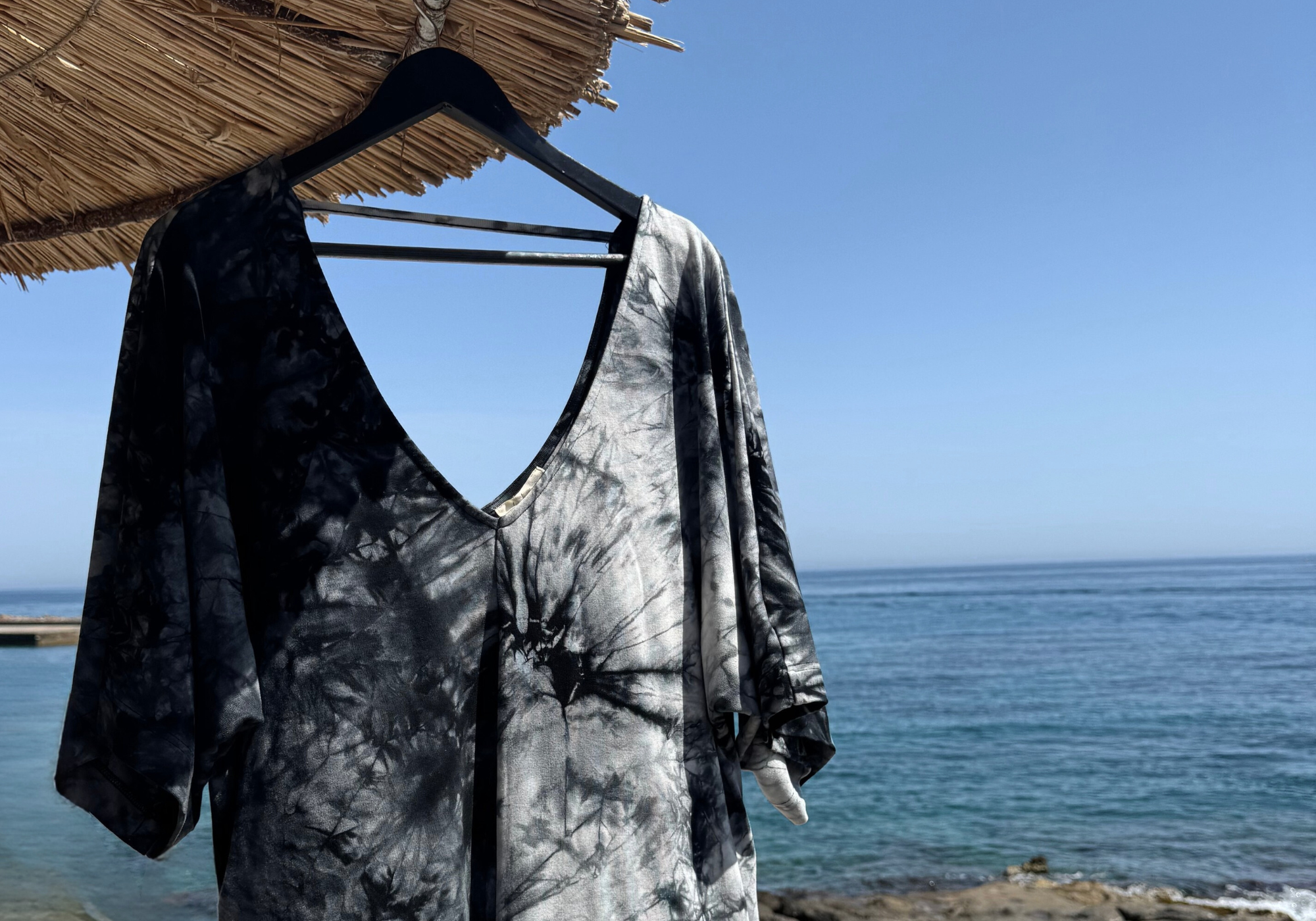Joplin Tie Dye batwing dress hanging from parasol in holiday beach setting.