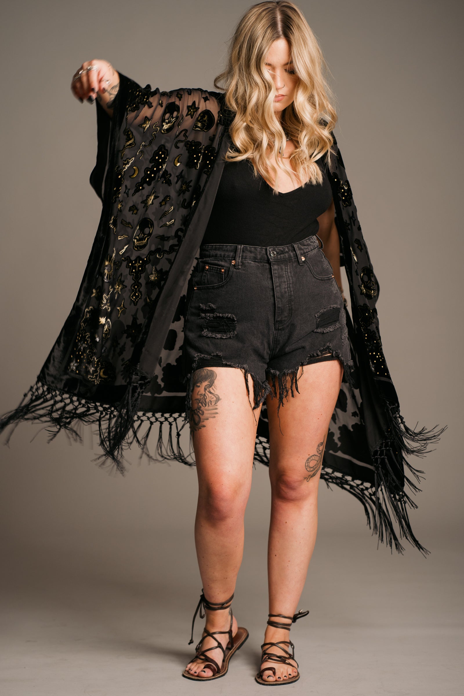 Model in studio wearing Suzi Skull Devore kimono with fringe detail. Styled with Denim shorts, and a cami top. The perfect Rock n Roll festival piece!
