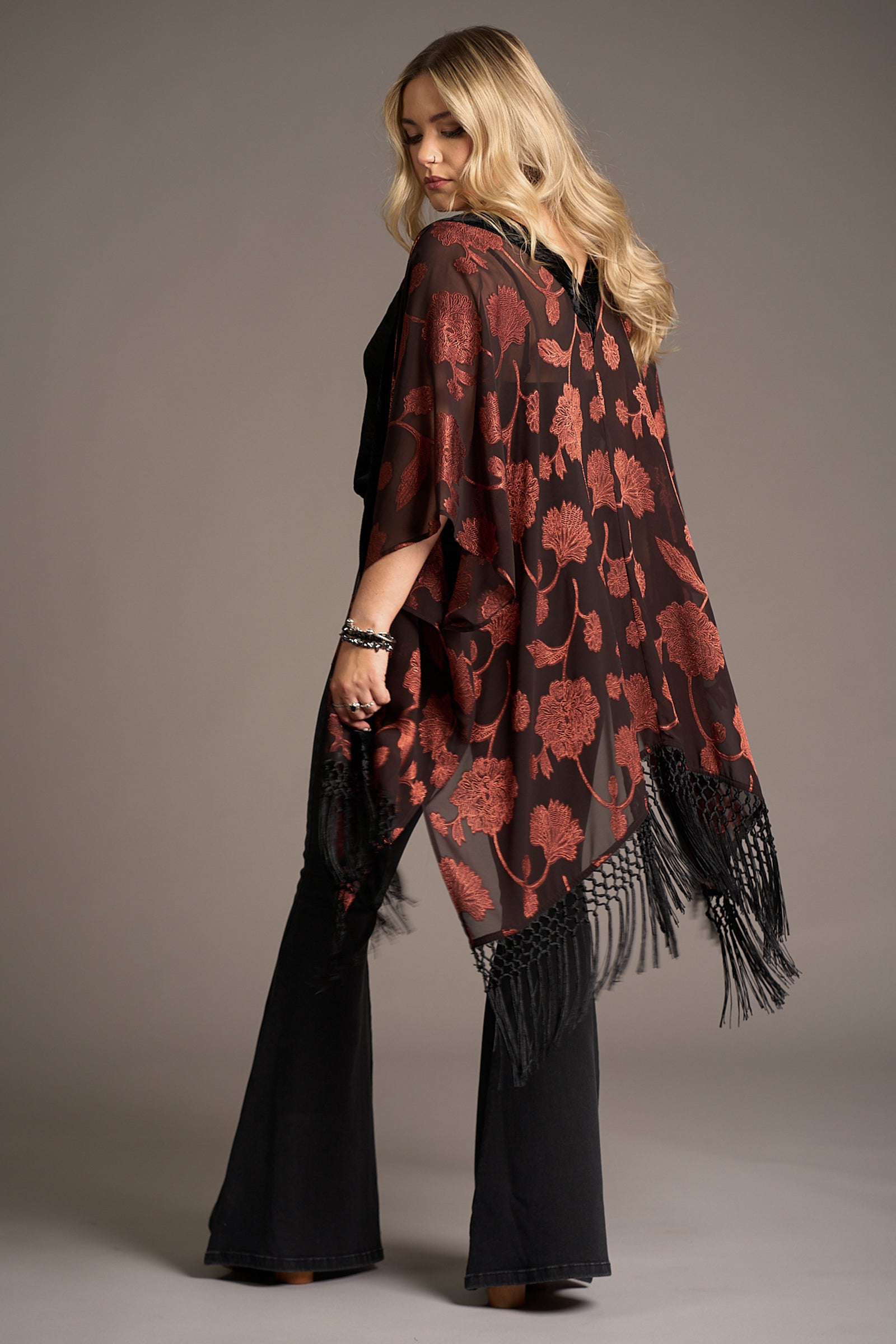 Erin showing the back of the Venus Fringed Kimono with black sheer fabric, red floral print, and fringe hem. Stevie Nicks inspired styling studio
