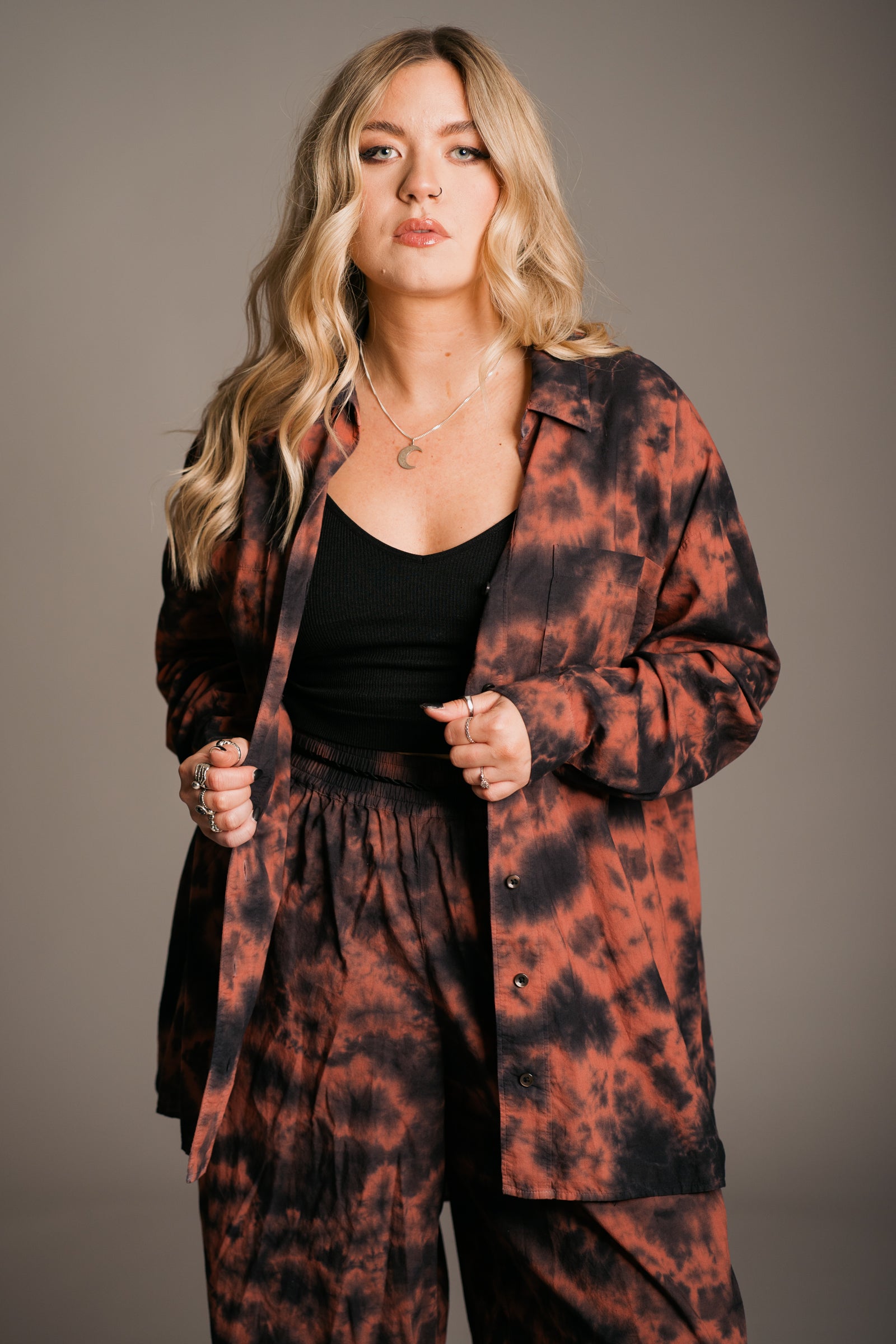 Model Erin wearing the Little Lies Zephyr Tie Dye Co-Ord, a vibrant tie-dye co-ord set featuring a relaxed-fit long-sleeve shirt worn open and matching wide-leg, tie-waist trousers. Styled with ankle-tie black sandals, the look embodies effortless bohemian style against a neutral backdrop.