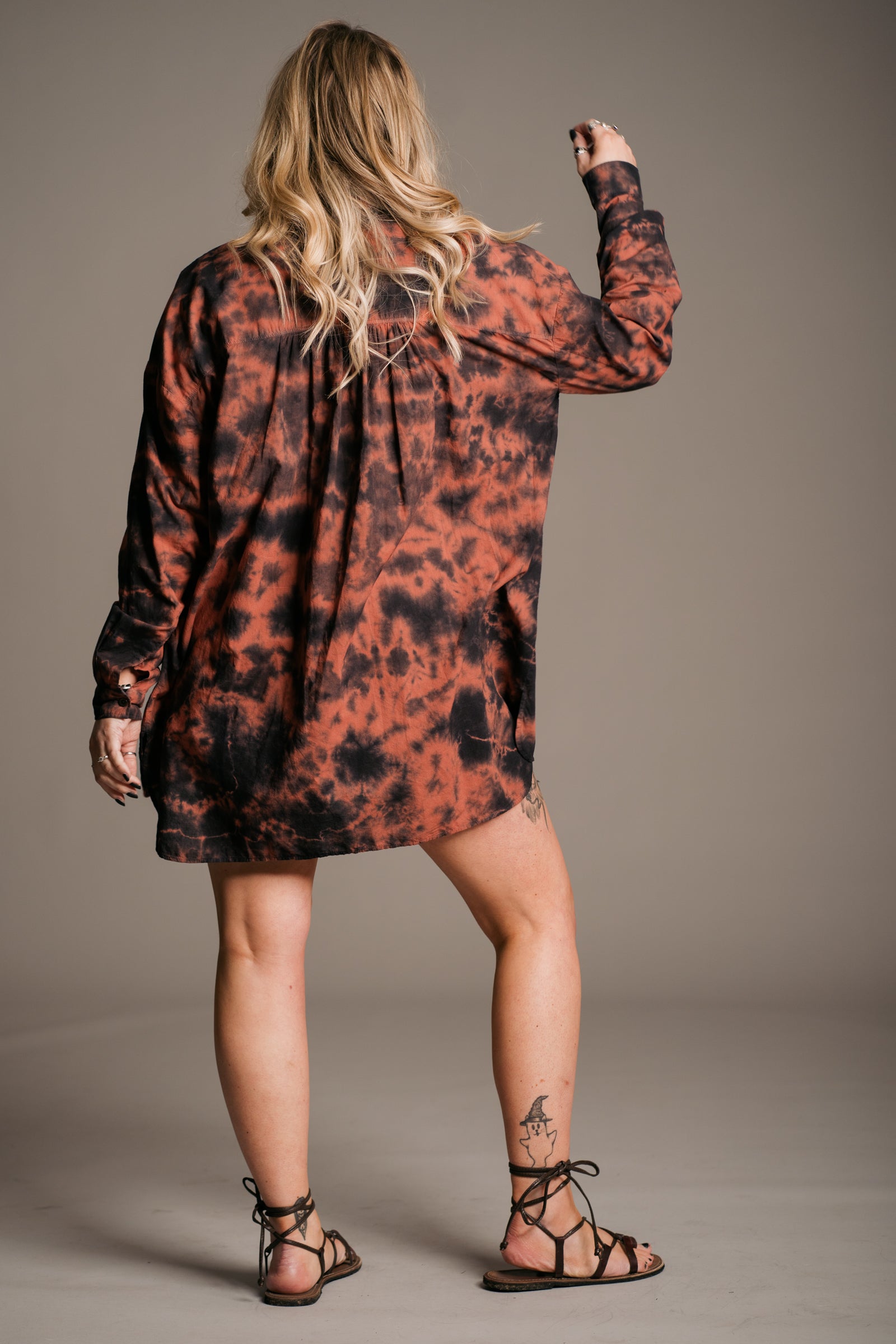 Model Erin wearing the Little Lies Zephyr Tie Dye Co-Ord Shirt, a vibrant tie-dye co-ord set featuring a relaxed-fit long-sleeve shirt showing the back. Styled with vintage distressed Levi's denim shorts, black vest top and ankle-tie black sandals, the look embodies effortless bohemian style against a neutral backdrop.