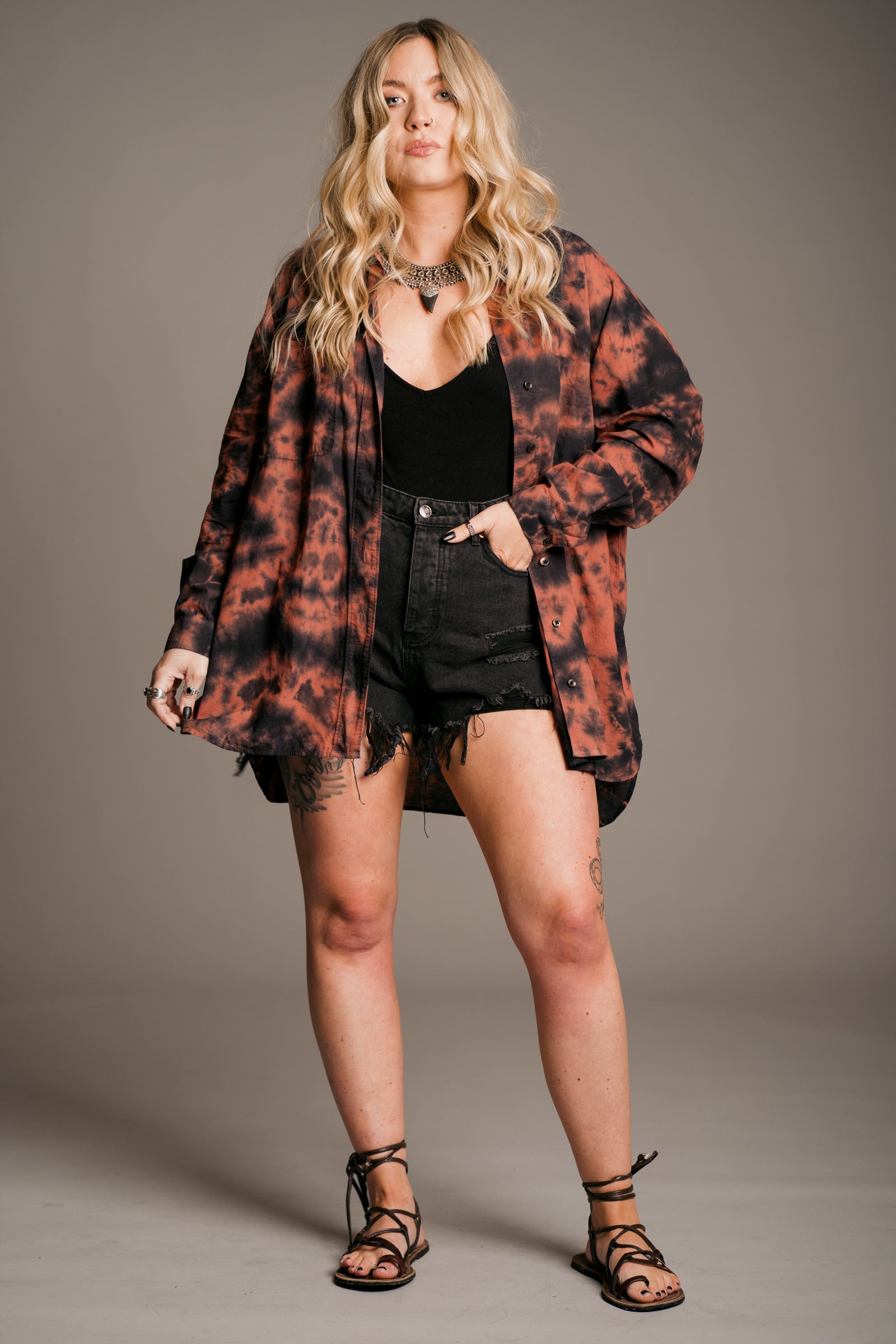 Model Erin wearing the Little Lies Zephyr Tie Dye Co-Ord Shirt, a vibrant tie-dye co-ord set featuring a relaxed-fit long-sleeve shirt. Styled with vintage distressed Levi's denim shorts, black vest top and ankle-tie black sandals, the look embodies effortless bohemian style against a neutral backdrop.