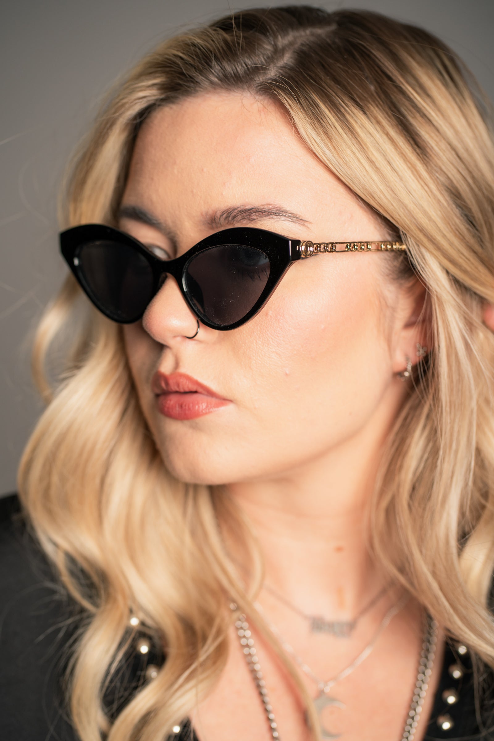 Little Lies Zoe black cat‑eye sunglasses with tinted lenses and gold chain arm detail, retro statement frame, on‑model close‑up view
