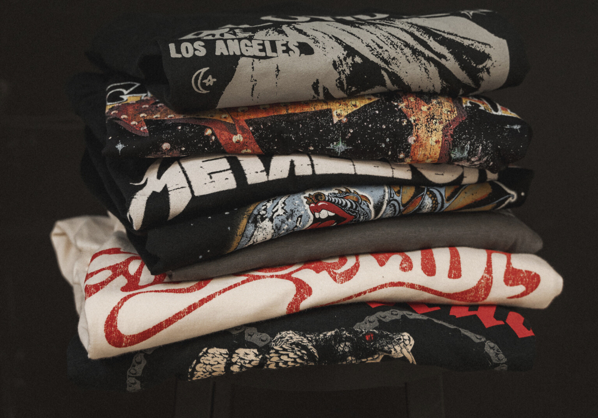 Little Lies stack of vintage-inspired band tees featuring graphic prints in black, grey, and white – folded on dark surface