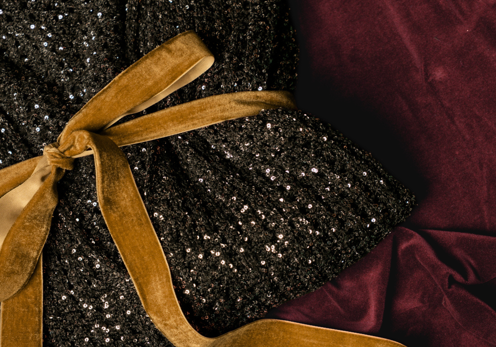 Close up of Little Lies Dazed & Confused Sequin Knit tied with yellow velvet ribbon, against a red velvet back drop