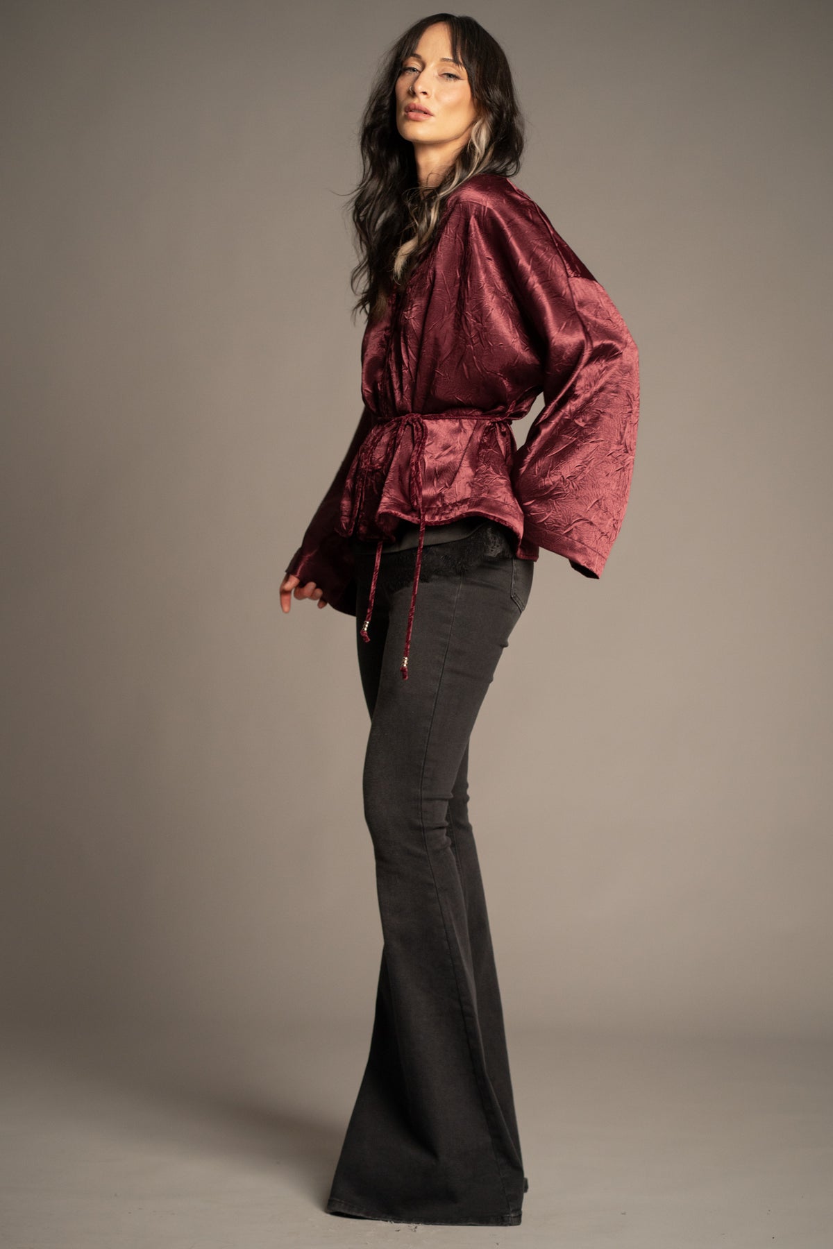 Celeste wine kimono top styled with black flared jeans, featuring a wrap front, wide sleeves and rich wine satin finish