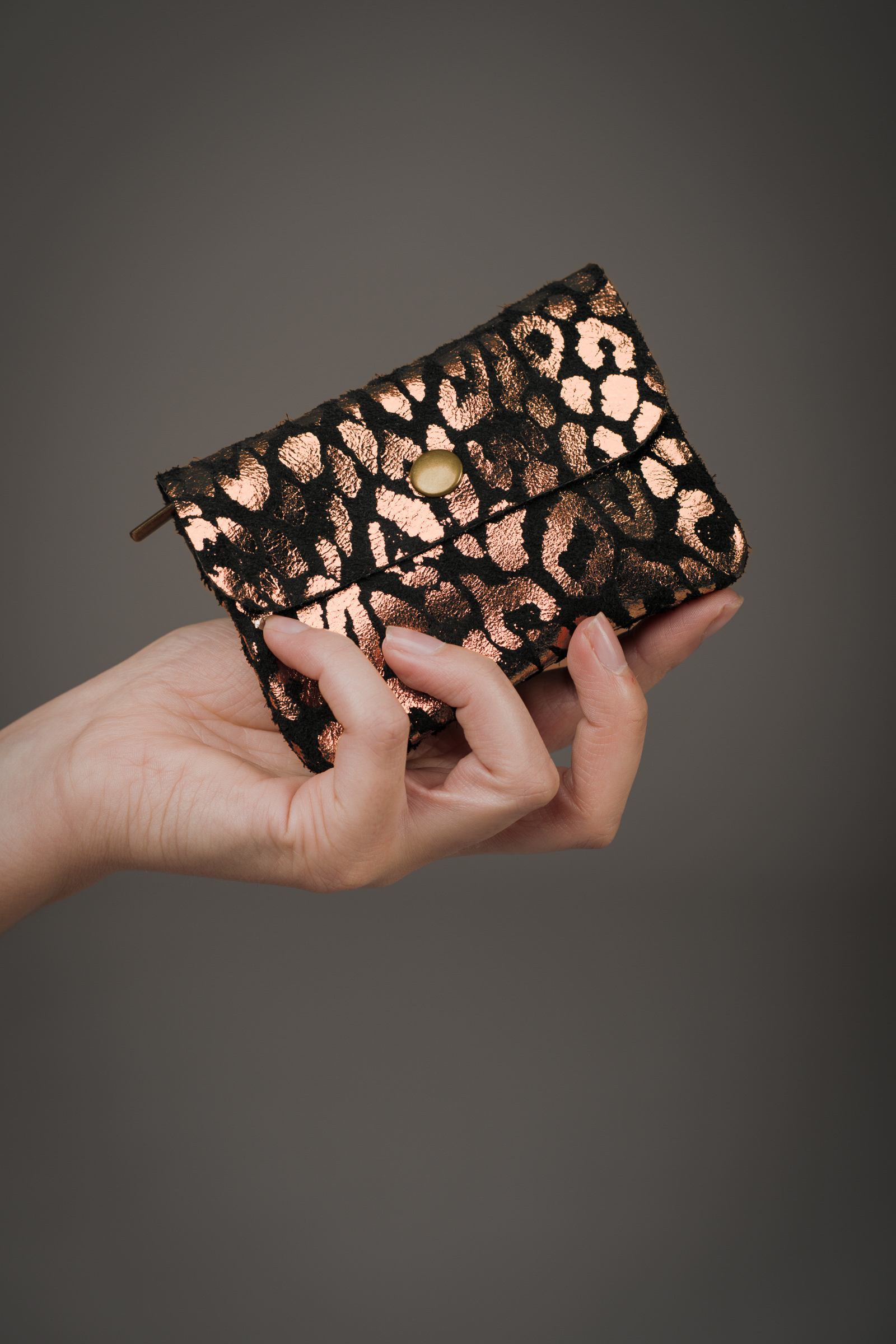 Copper metallic genuine suede purse with black animal‑print overlay held in a hand against a grey background.