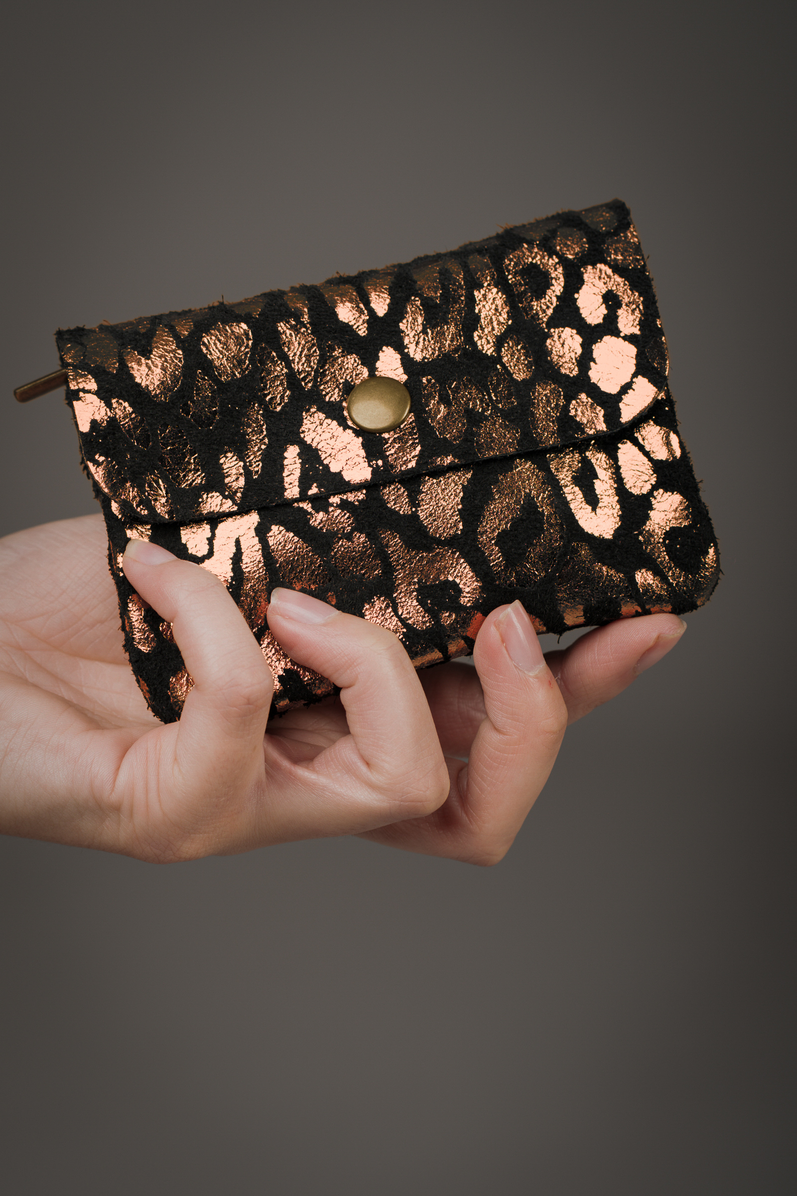 Copper metallic genuine suede purse with black animal‑print overlay held in a hand against a grey background.