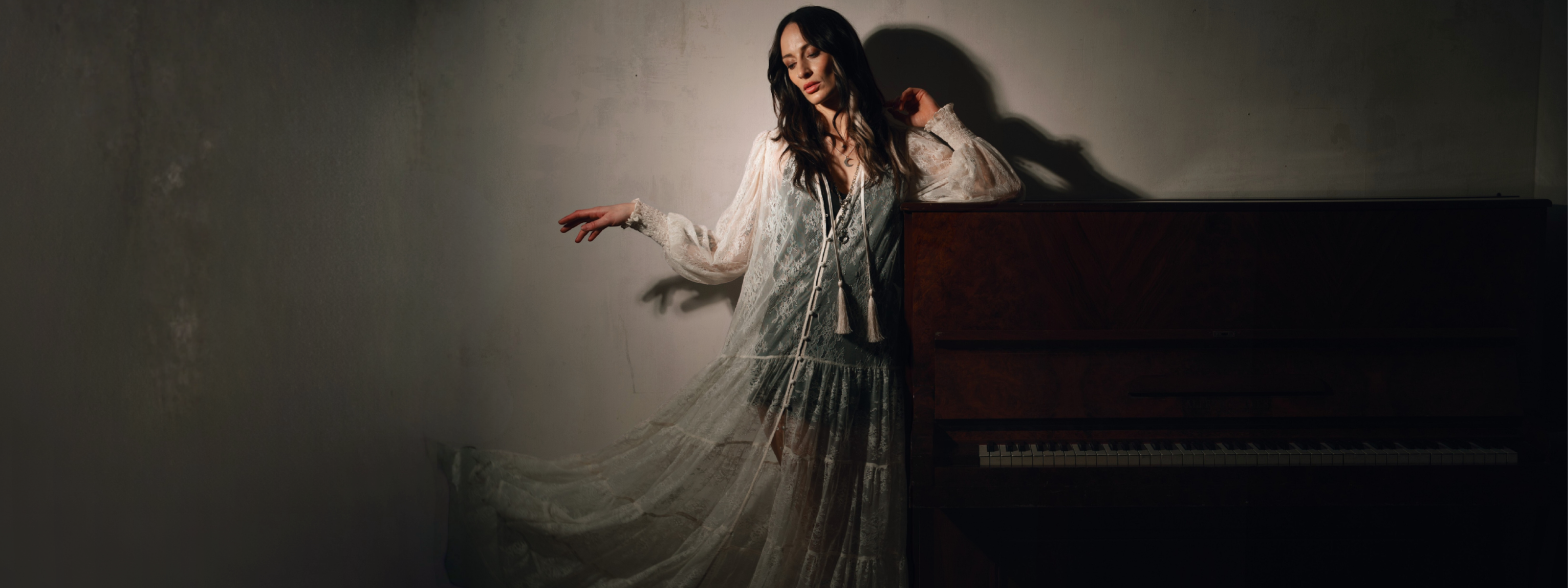 Model wearing the Little Lies Rhiannon Ivory Maxi Dress featuring sheer ivory lace fabric, long voluminous sleeves, tassel ties, and a tiered maxi‑length skirt worn over the Nightbird Satin Slip Dress as an underlayer.