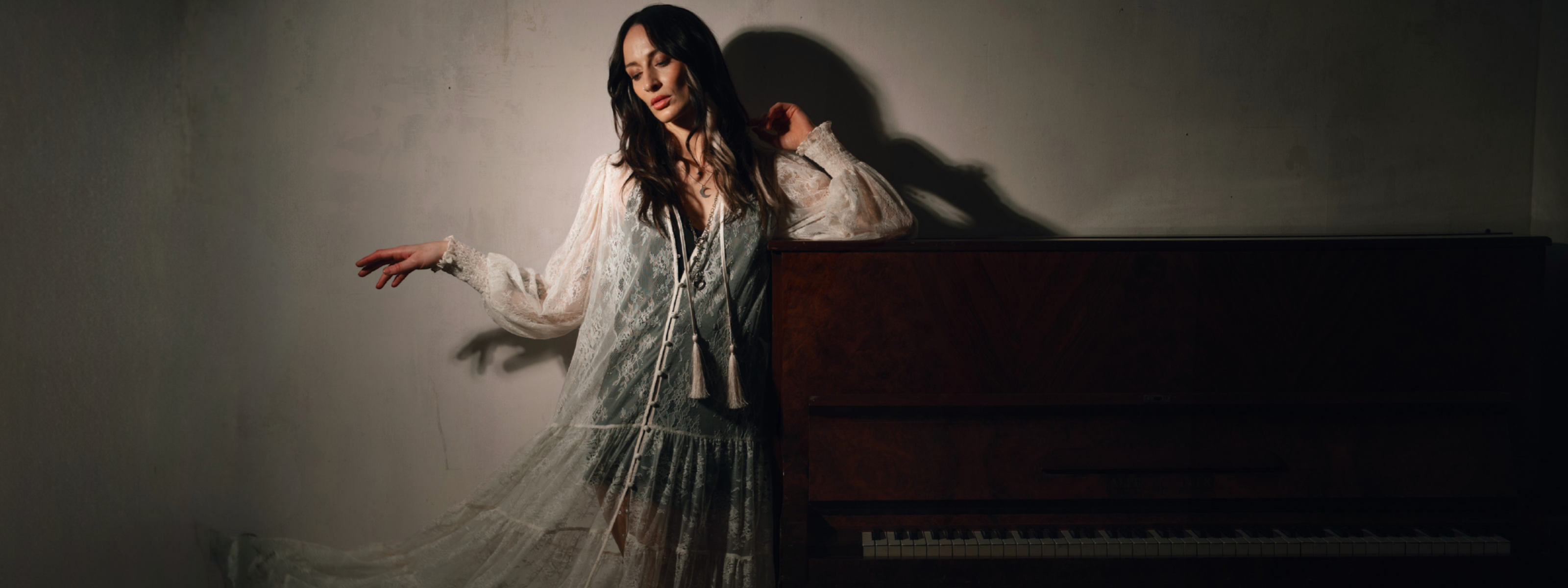 Model wearing the Little Lies Rhiannon Ivory Maxi Dress featuring sheer ivory lace fabric, long voluminous sleeves, tassel ties, and a tiered maxi‑length skirt worn over the Nightbird Satin Slip Dress as an underlayer.