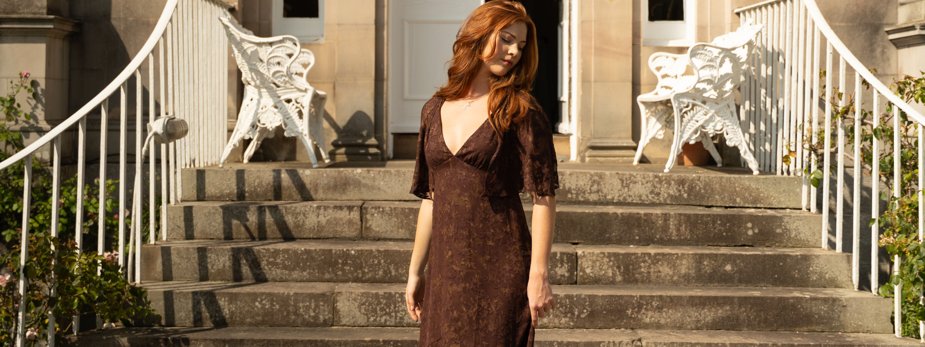 Model wearing Brown Sugar Chiffon Midi Dress from Little Lies featuring sheer flutter cape sleeves, a deep V‑neckline, and tonal floral chiffon shown in a full‑length.