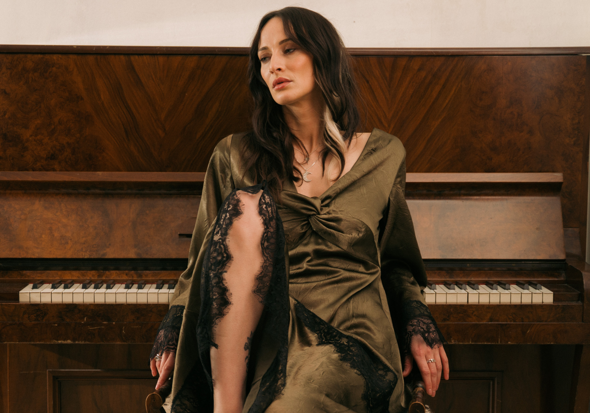 model leaning back on piano wearing Little Lies Arabella Satin Maxi Dress with black lace trim.