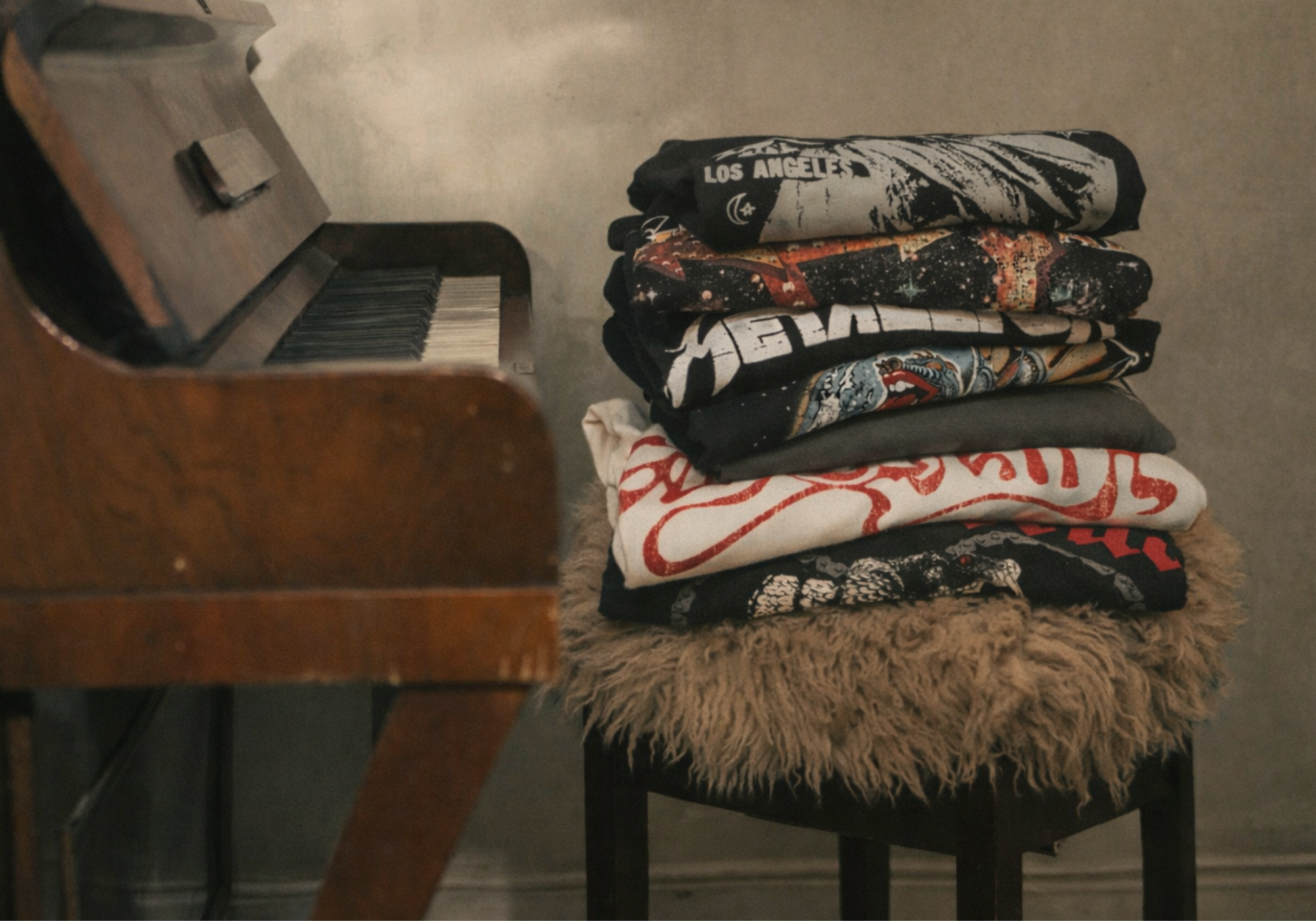 Little Lies stack of vintage-inspired band tees featuring graphic prints in black, grey, and white – folded on piano chair
