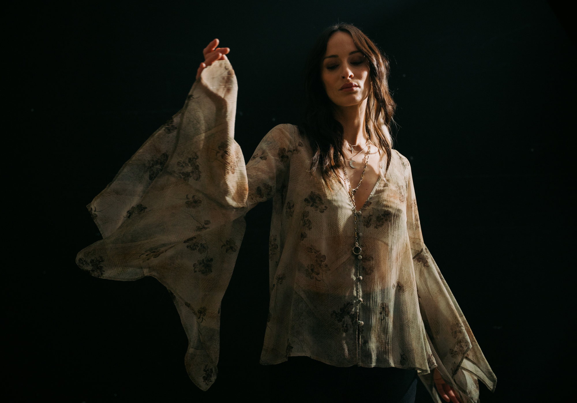 Model wearing the Little Lies Karma Sage Blouse in soft sage floral print with flowing asymmetric sleeves.