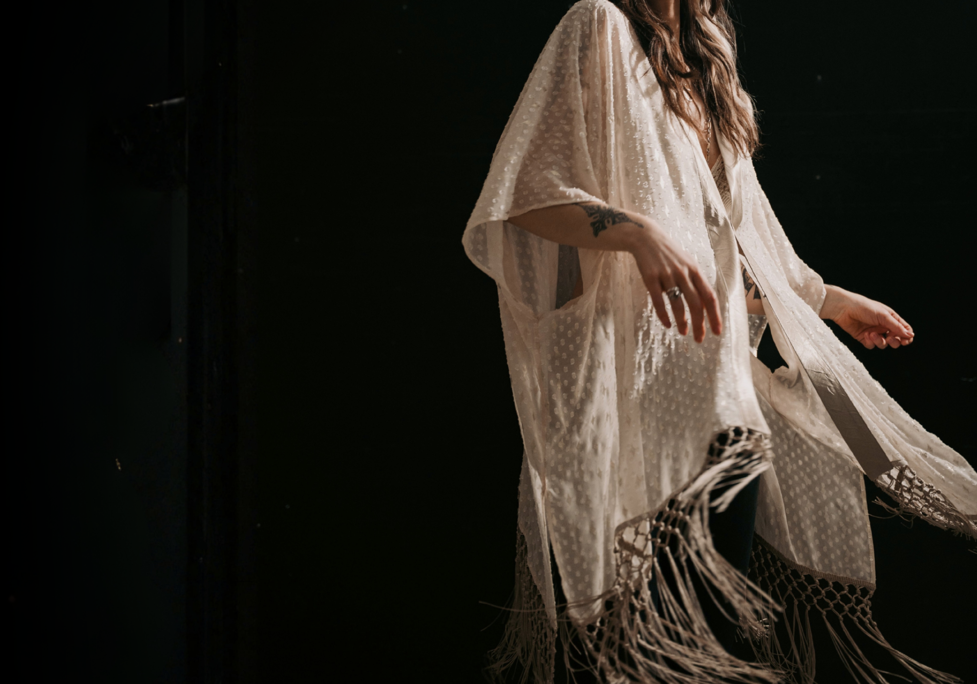 Headless shot of model wearing the Little Lies Songbird Ivory Kimono featuring a soft ivory draped fabric with subtle textured detailing and long fringe trim.