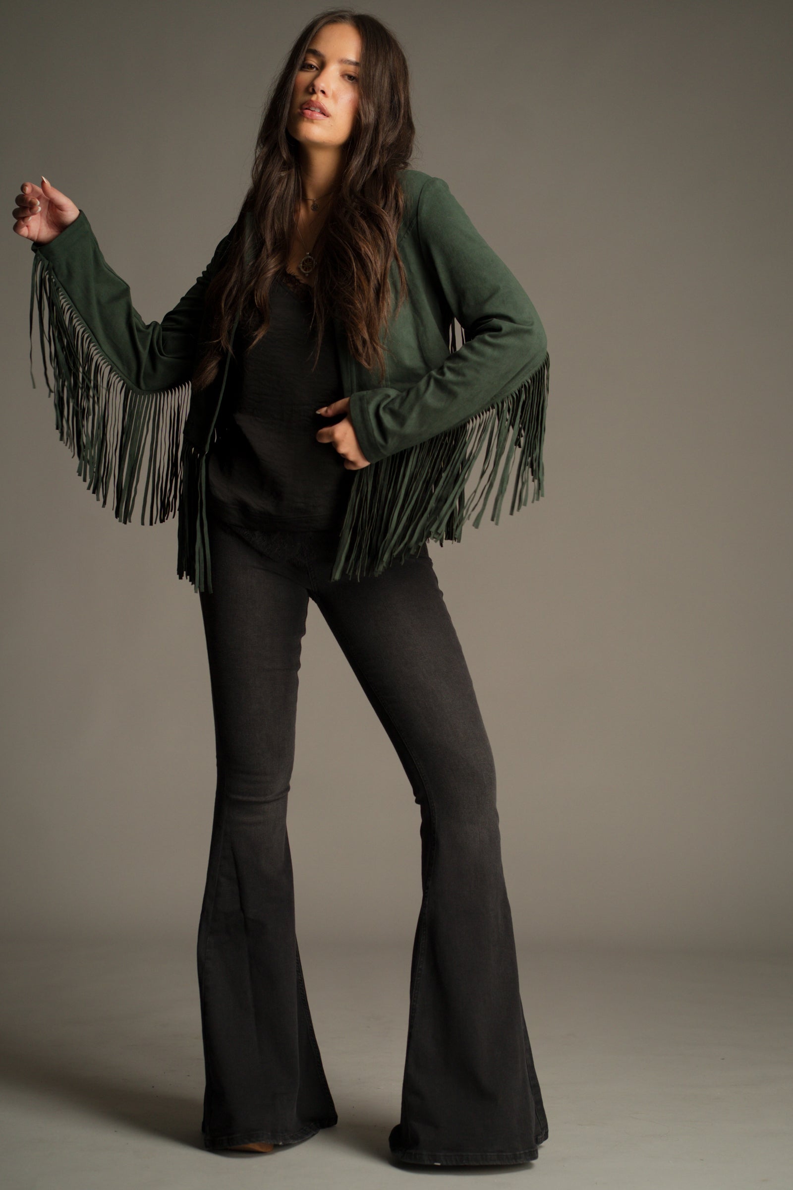 Front view of the Ivy Emerald Green Fringed Faux Suede Jacket in deep emerald with dramatic fringe. Styled with Hendrix Denim Flares.