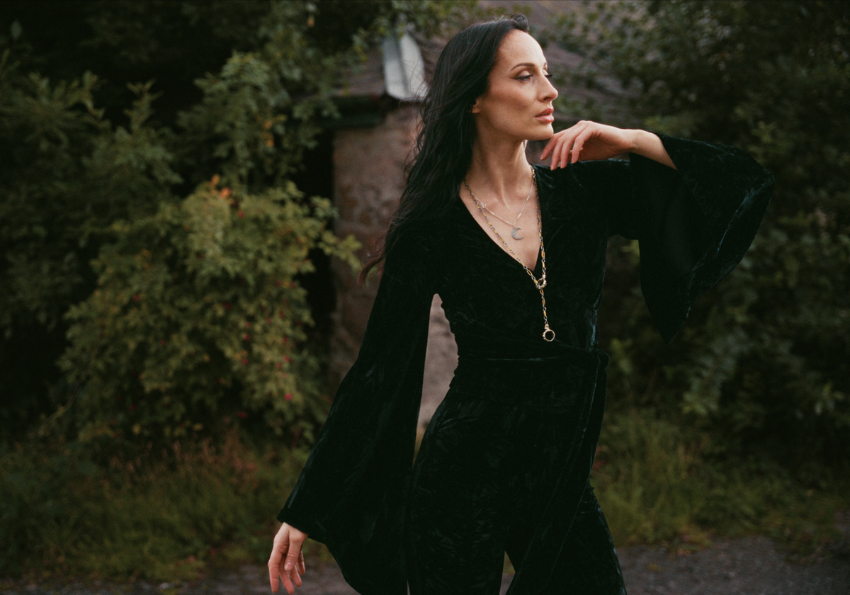 Model wearing the Little Lies Sally Black Velvet Wrap Top with dramatic bell sleeves in an outdoor Spellbound campaign shoot.