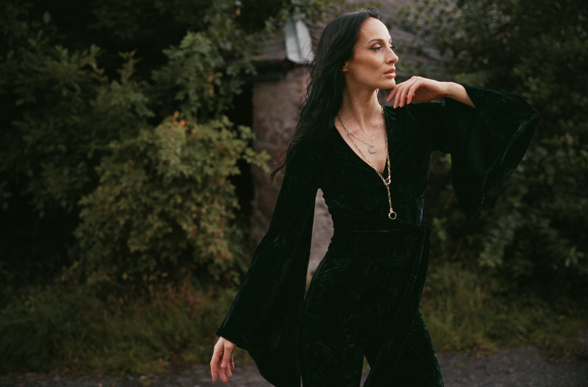 Model wearing the Little Lies Sally Black Velvet Wrap Top with dramatic bell sleeves in an outdoor Spellbound campaign shoot.