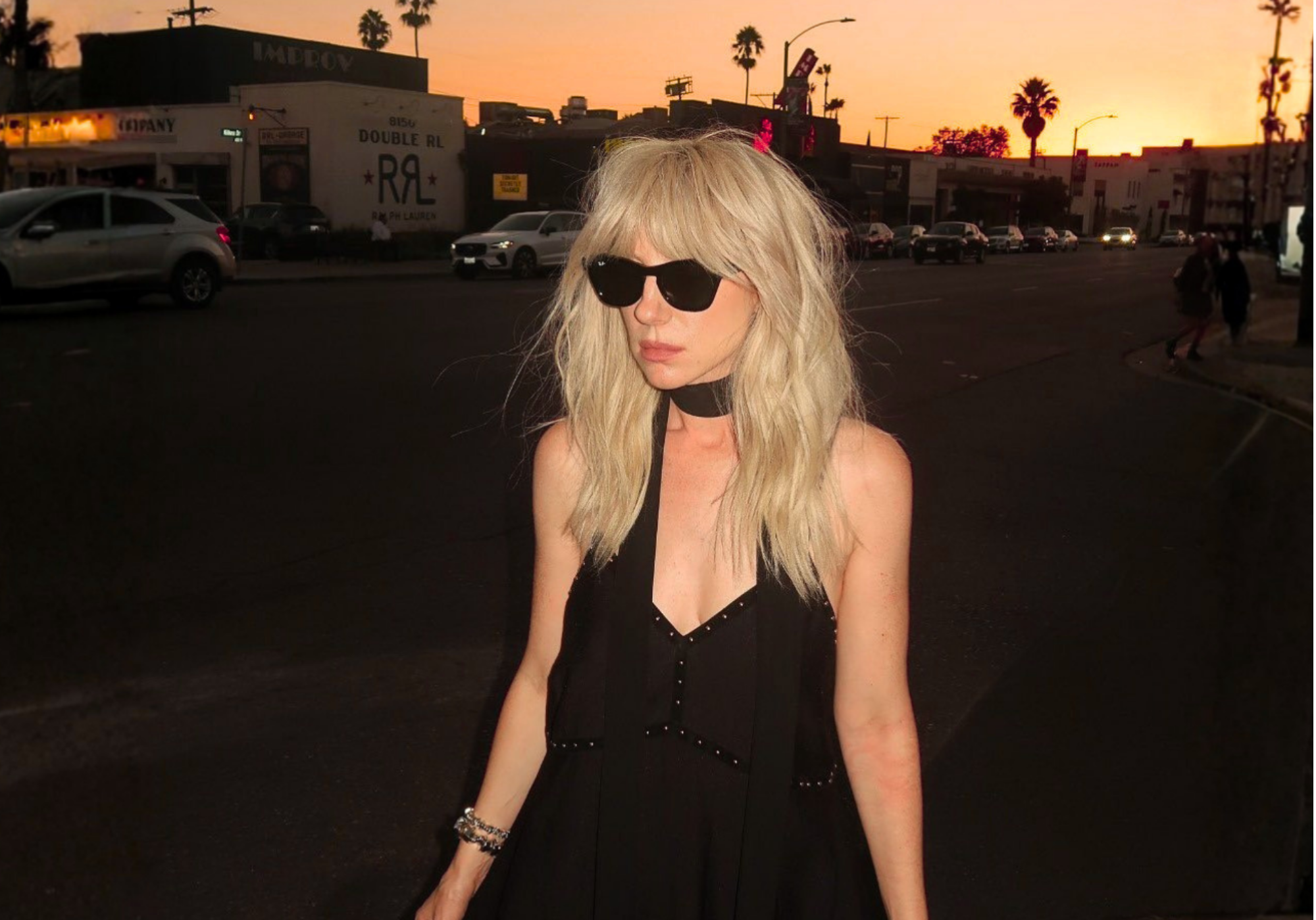 Shop the Little Lies Sale Collection with up to 60% off. Model wearing the Landslide Studded Slip Dress and sunglasses with LA sunset background.