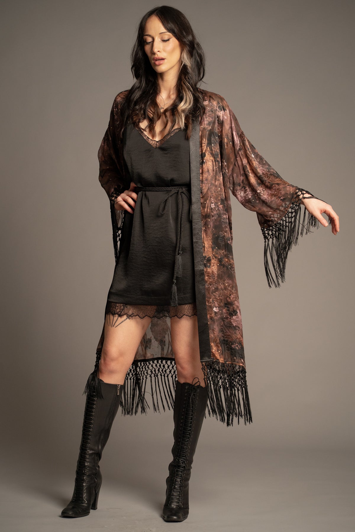 Practical Magic kimono styled over a black lace-trim mini dress with knee-high boots, featuring floral print and tassel fringe