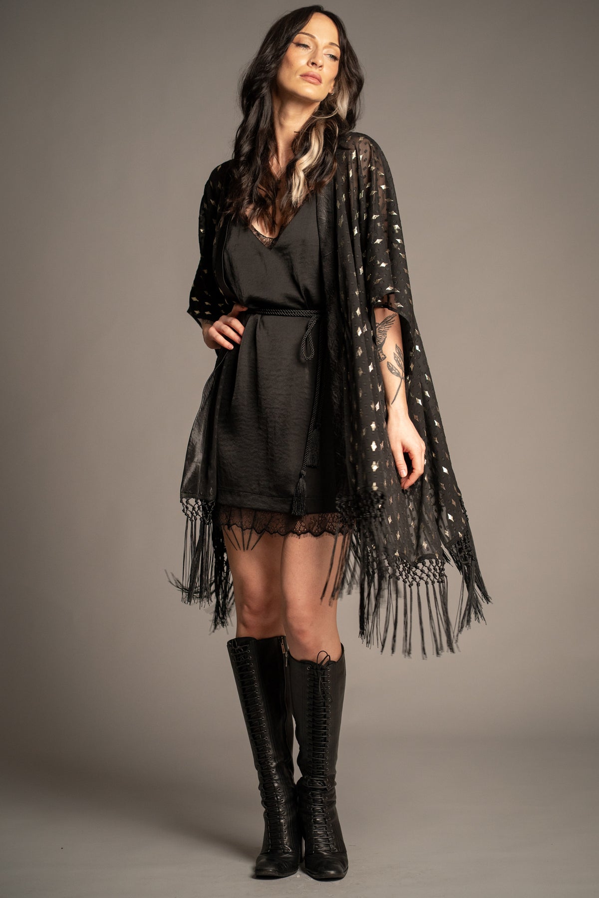 Songbird black metallic kimono styled over a black mini dress with knee-high boots, featuring gold foil stars and tassel fringe hem