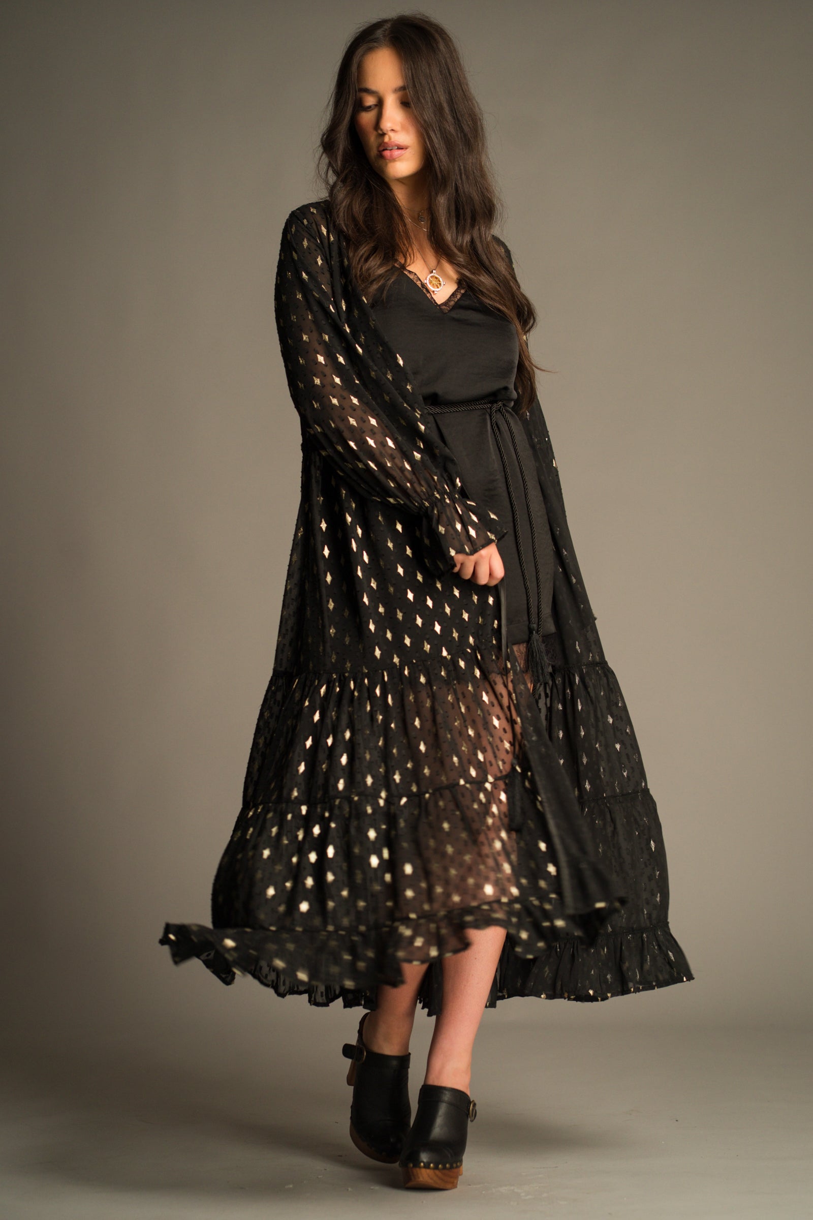 Space Oddity Metallic Maxi Dress by Little Lies styled over a black slip dress, featuring sheer metallic fabric, a flowing bohemian silhouette and shimmering gold foil detailing
