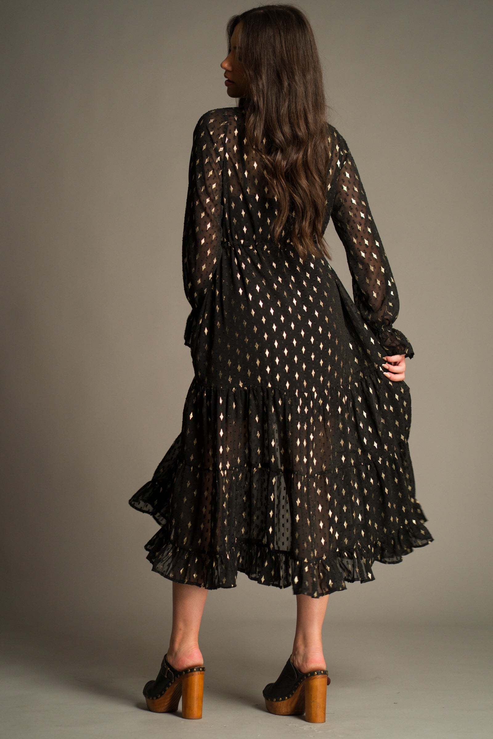 Back view of the Space Oddity Metallic Maxi Dress showcasing the flowing tiered skirt, sheer long sleeves and all-over metallic foil detailing