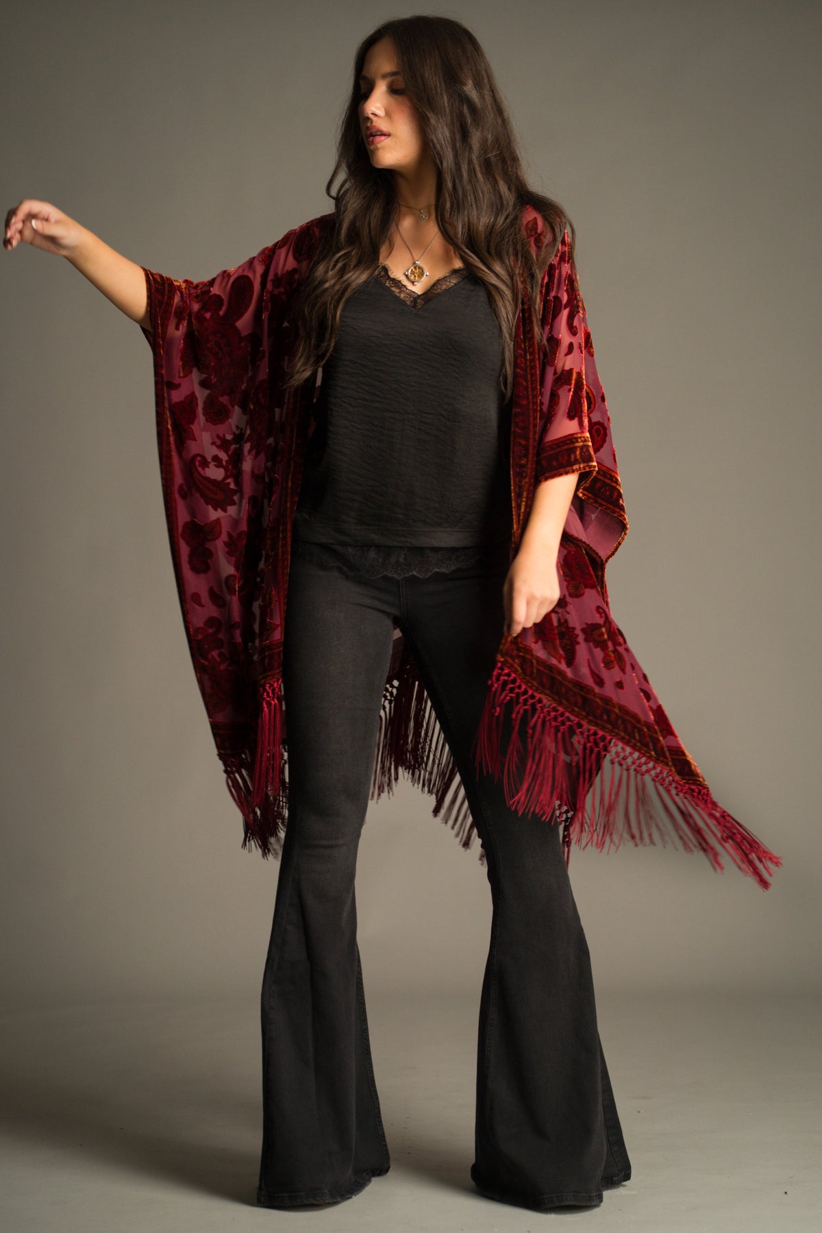 Jess wears Little Lies Stevie Plum Paisley Devore Kimono in rich plum with velvet paisley pattern and long fringing, styled over black satin cami and denim flares.