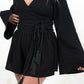 Model wearing Woodstock Wrap Top - Black True wrap top with double tassel tie detail and flared sleeve