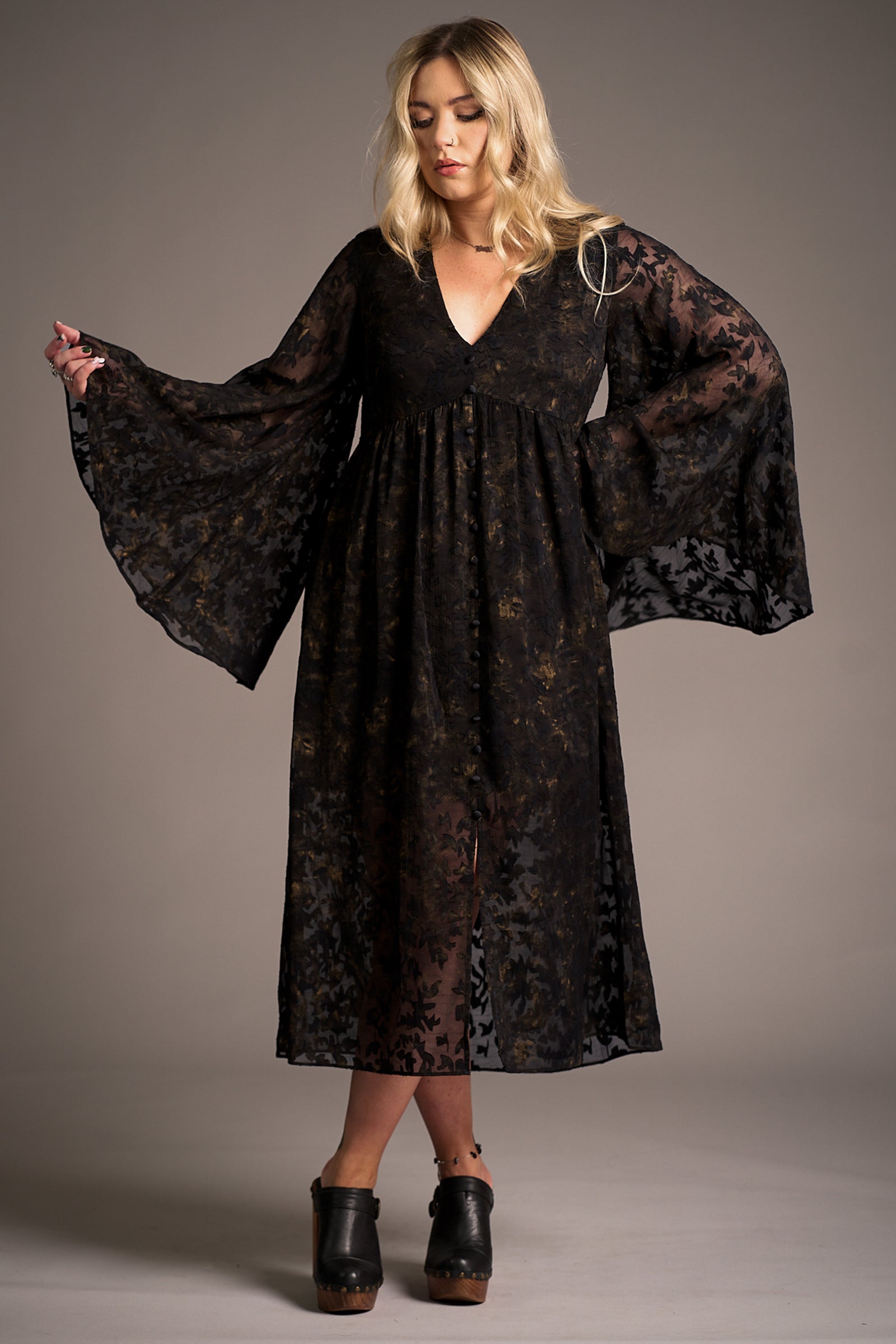Erin wears the Bella Donna Midi Dress featuring sheer black floral overlay and bell sleeves against a neutral backdrop, Stevie Nicks inspired styling studio