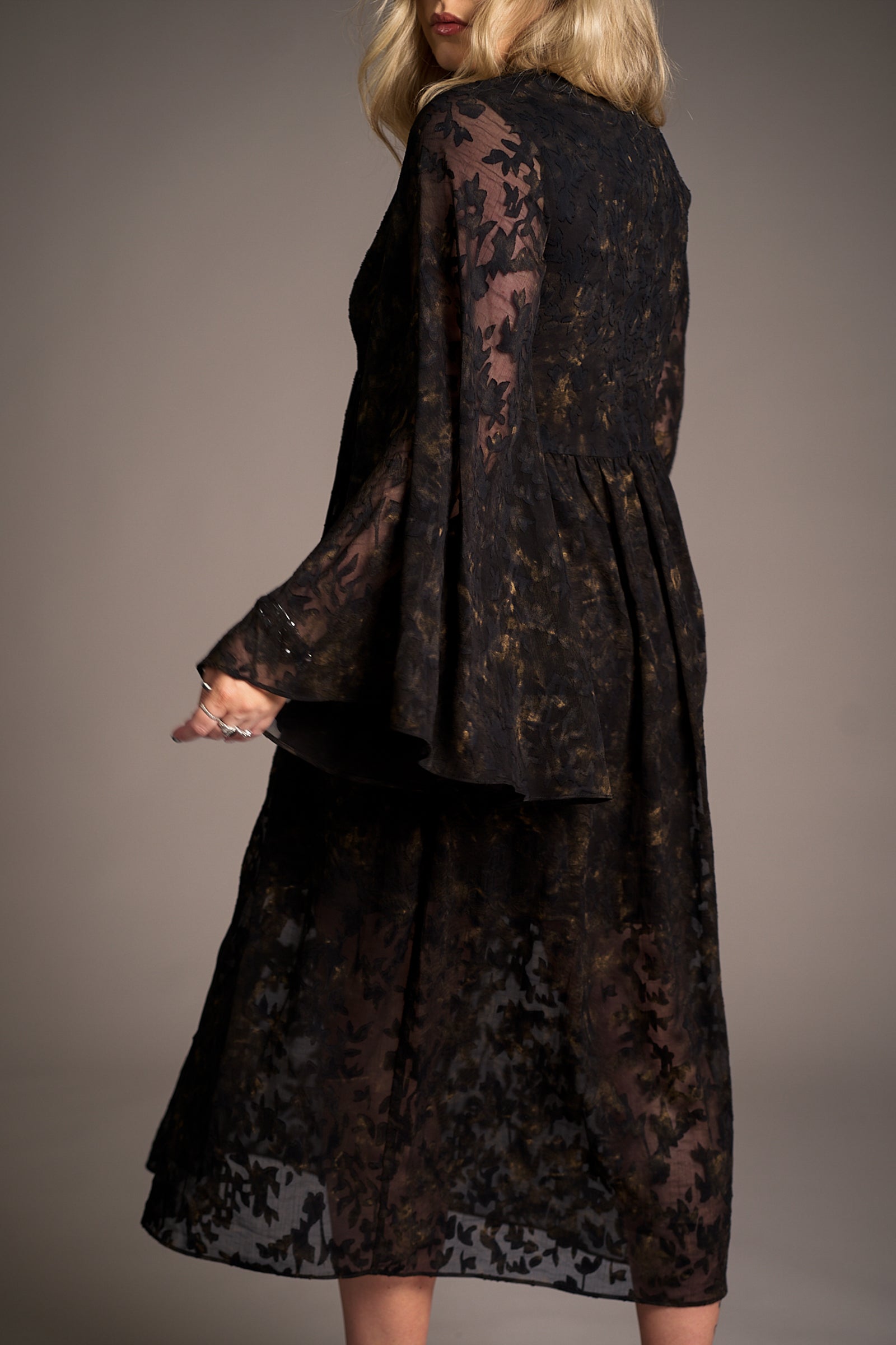 Side view of Erin wearing the Bella Donna Midi Dress in sheer black fabric with intricate floral patterns and flared sleeves, Stevie Nicks inspired styling studio