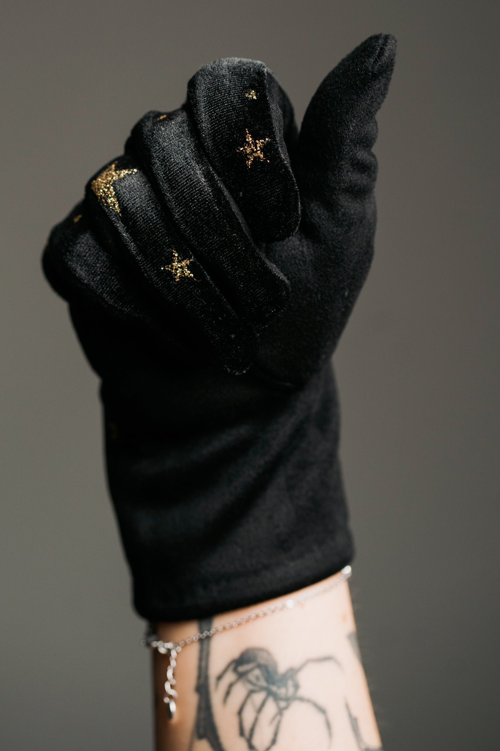 Close-up product shot showcasing the Black Velvet Celestial Gloves, smooth black fabric with gold star print detail.