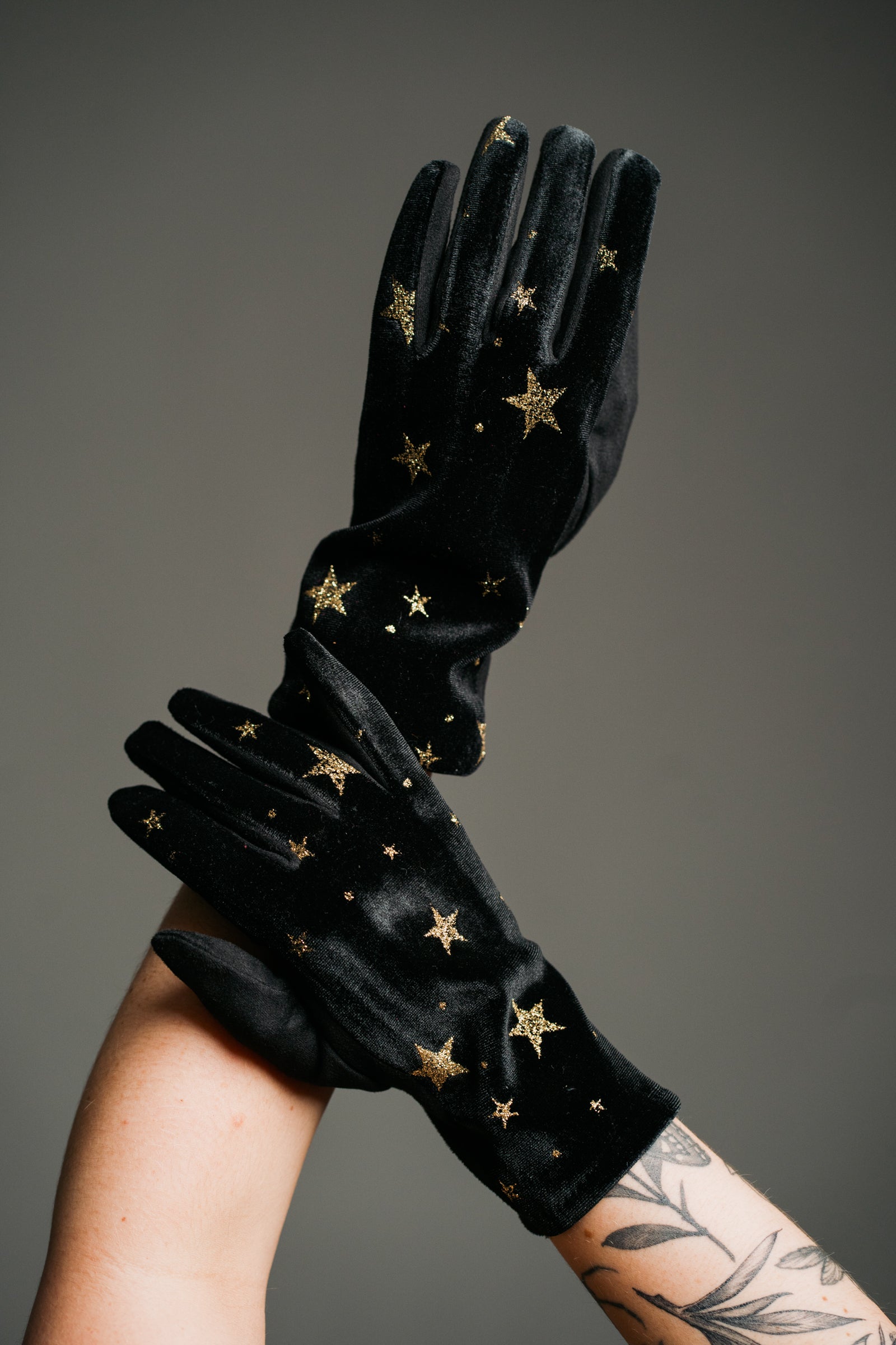 Product shot showcasing the Black Velvet Celestial Gloves, smooth black fabric with gold star print detail.