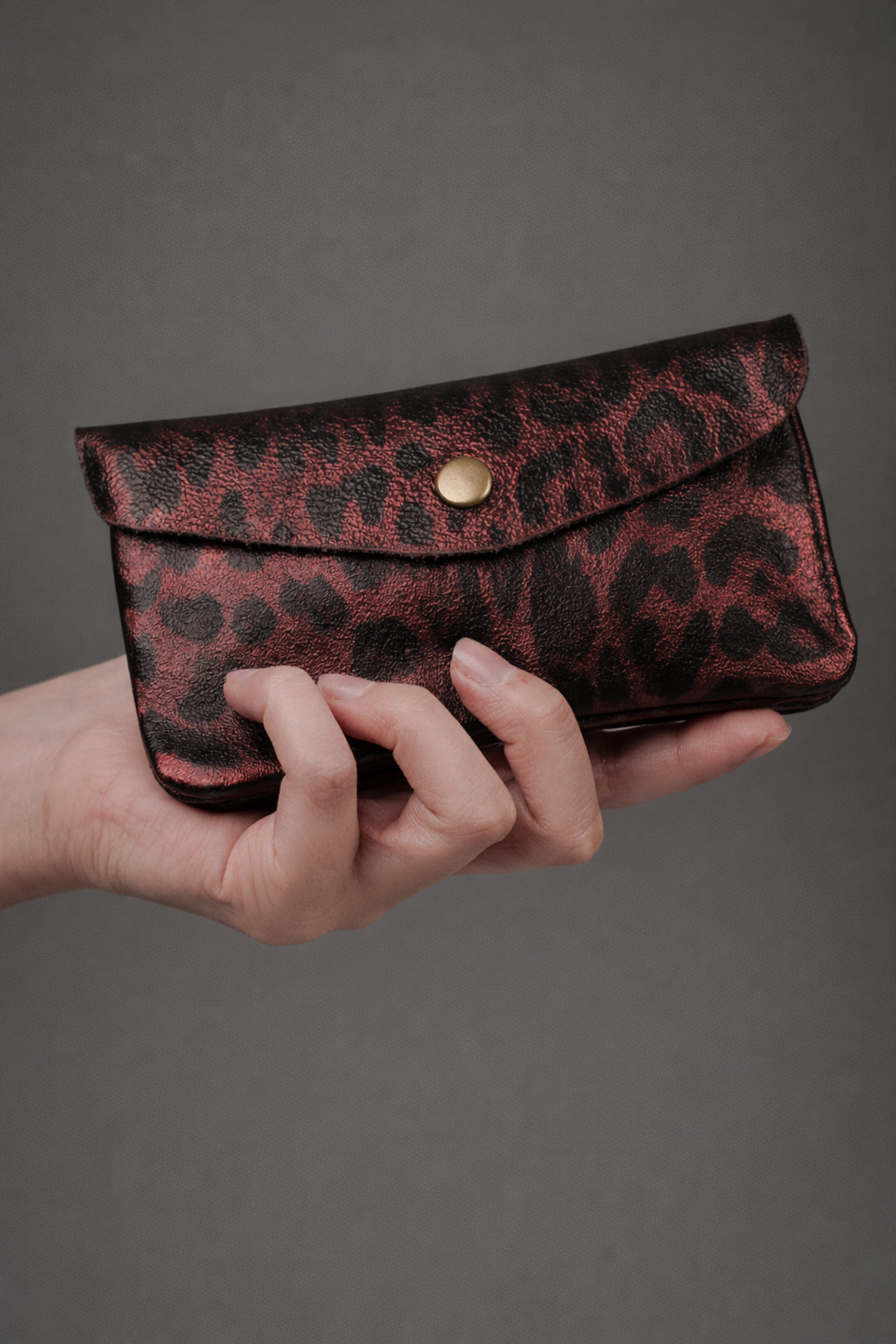 Cherry red metallic genuine suede purse with leopard print pattern held in a hand.