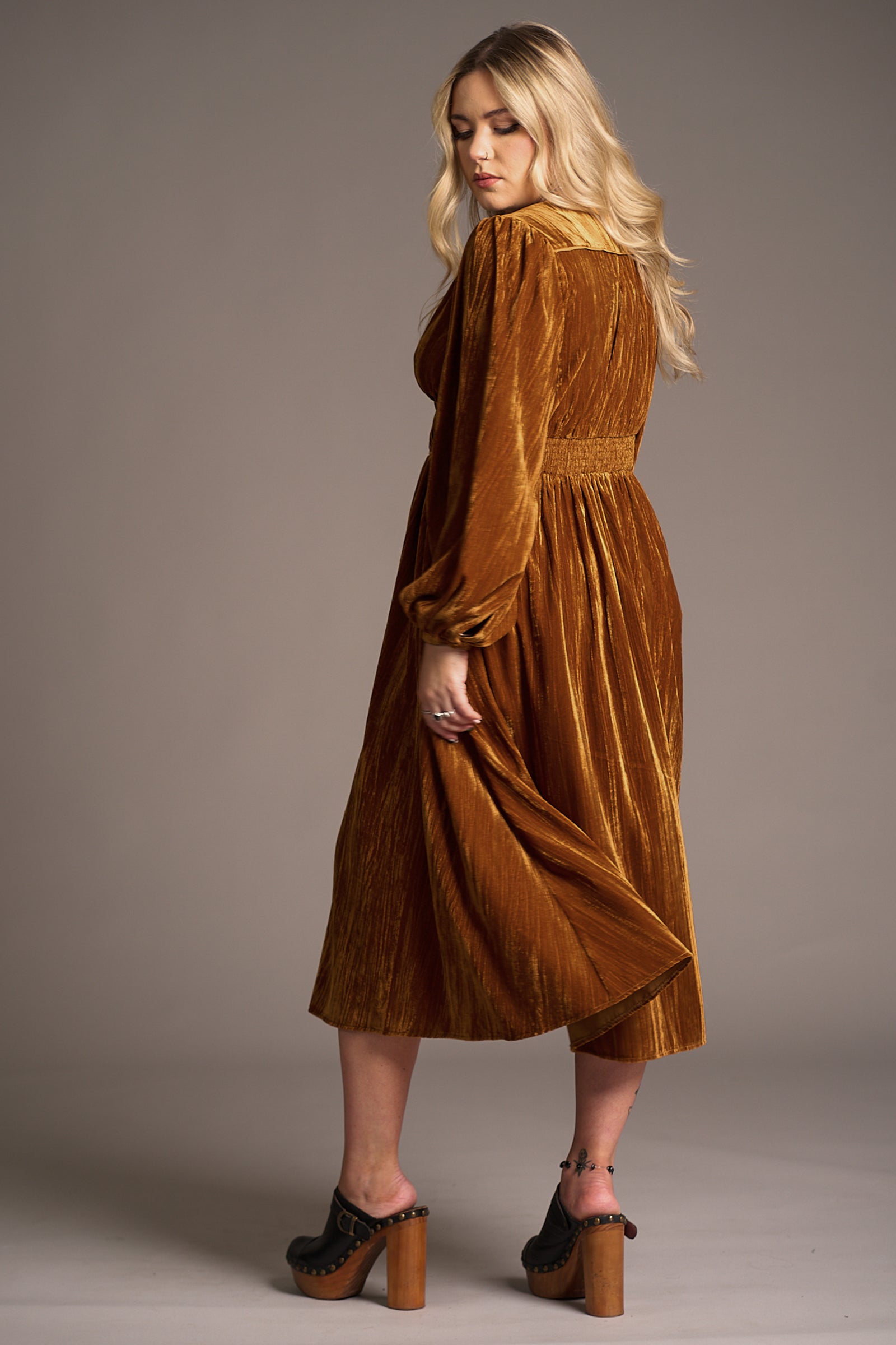 Back view of Erin in Dazed Copper Velvet Midi Dress with flowing silhouette and platform heels, styled in studio shoot, Stevie Nicks inspired styling