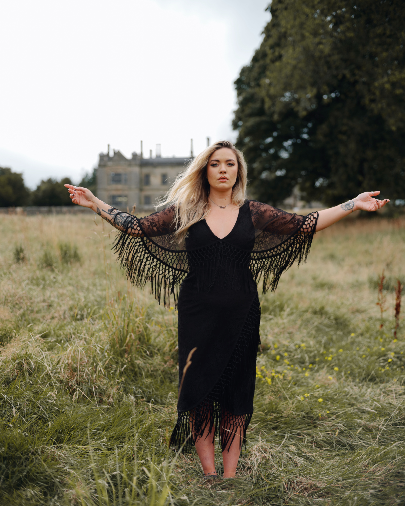 Erin wears Tango in the Night Lace Midi Dress, Stevie Nicks inspired styling, outdoor, set against a vintage manor and wild grass.