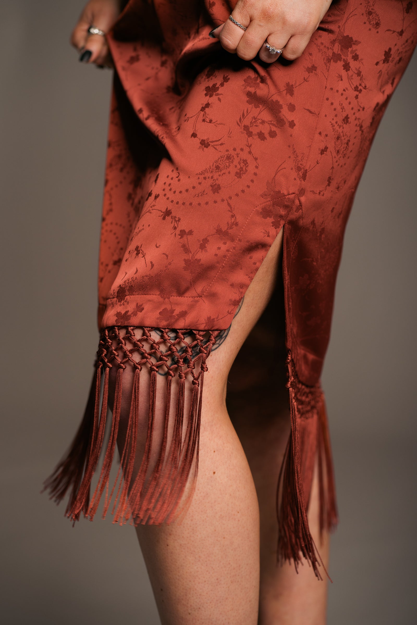 Our Model, Erin,  posing against a neutral backdrop, wearing the Little Lies Florence Rust Satin Fringed Kimono Dress with side split and details and rust fringing around the hem. Perfect relaxed bohemian style. 