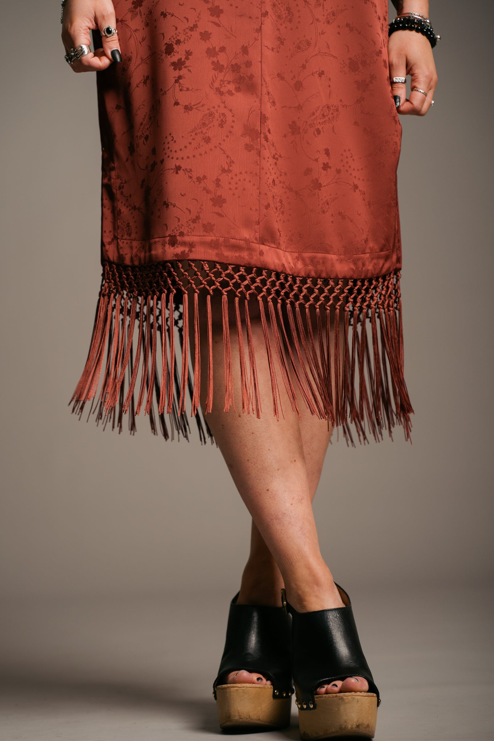 Our Model, Erin,  posing against a neutral backdrop, wearing the Little Lies Florence Rust Satin Fringed Kimono Dress with side split and details and rust fringing around the hem. Perfect relaxed bohemian style. 