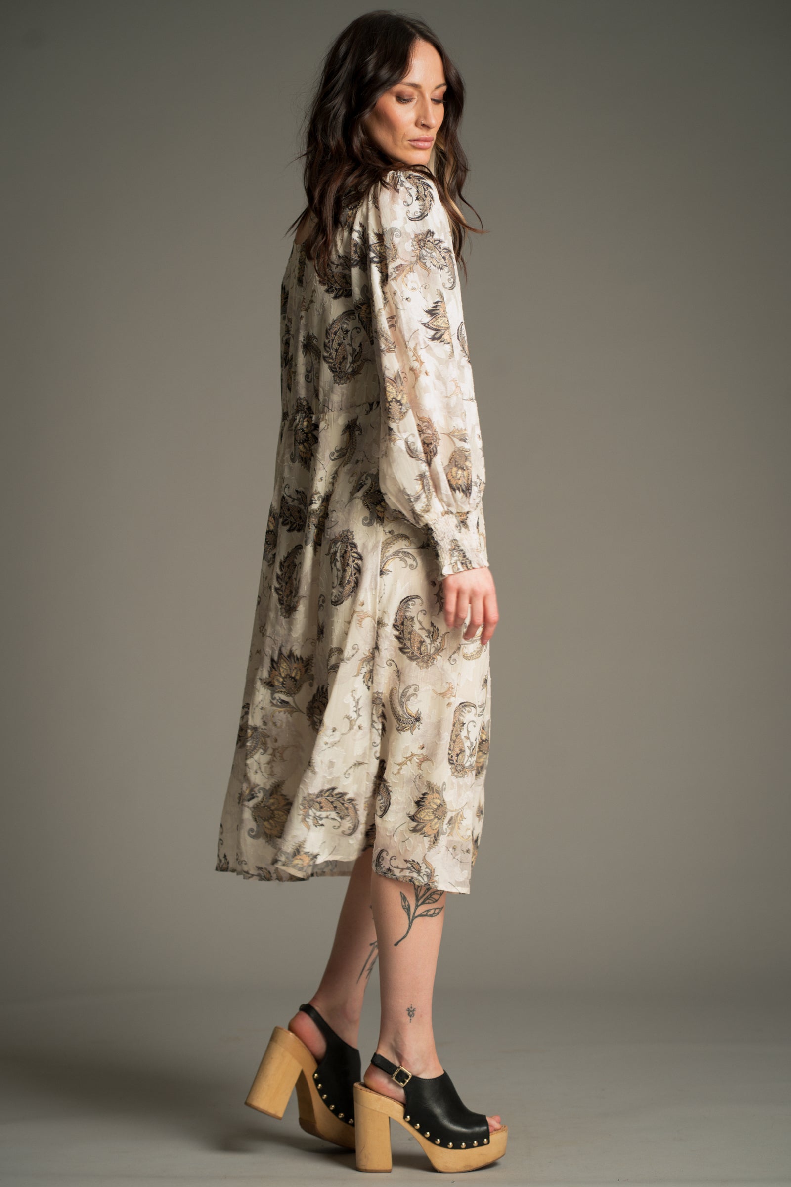 Victoria wears Little Lies Harvest Moon Paisley Midi Dress in cream with an intricate paisley print, side view showing long voluminous sleeves and flowing midi silhouette, styled with platform sandals.