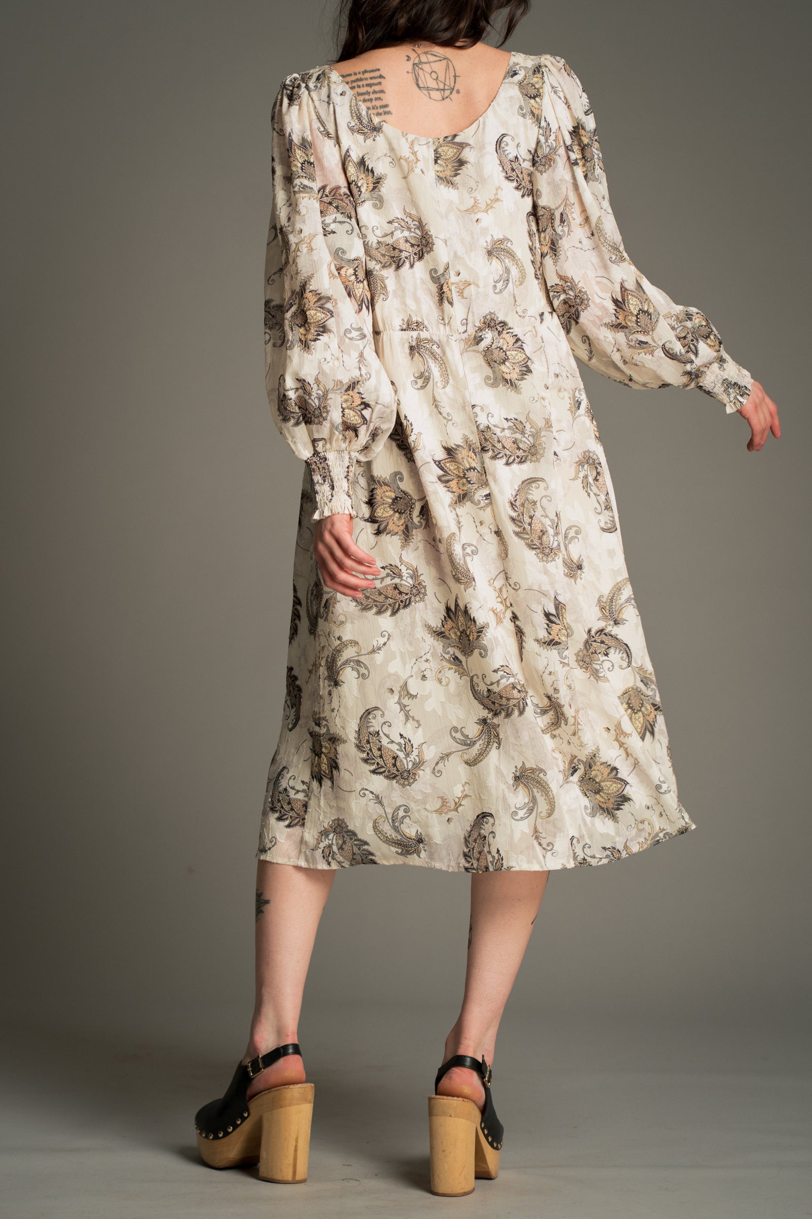 Little Lies Harvest Moon Paisley Midi Dress in cream with an intricate paisley print, back view showing long gathered sleeves and a flowing midi silhouette, styled with platform sandals.