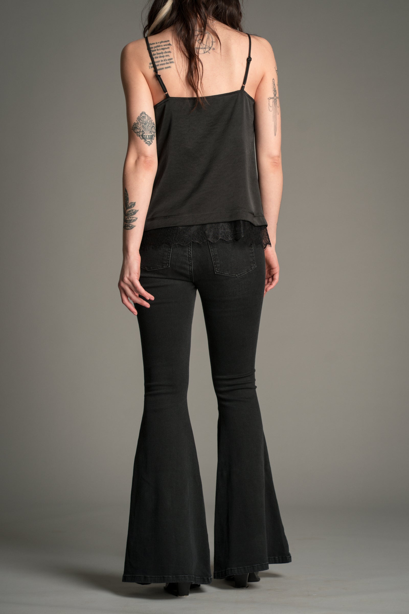 Little Lies Hendrix Denim Flares in washed black denim, back view showing high‑waist fit, rear patch pockets, and wide flared legs, styled with a black satin cami.