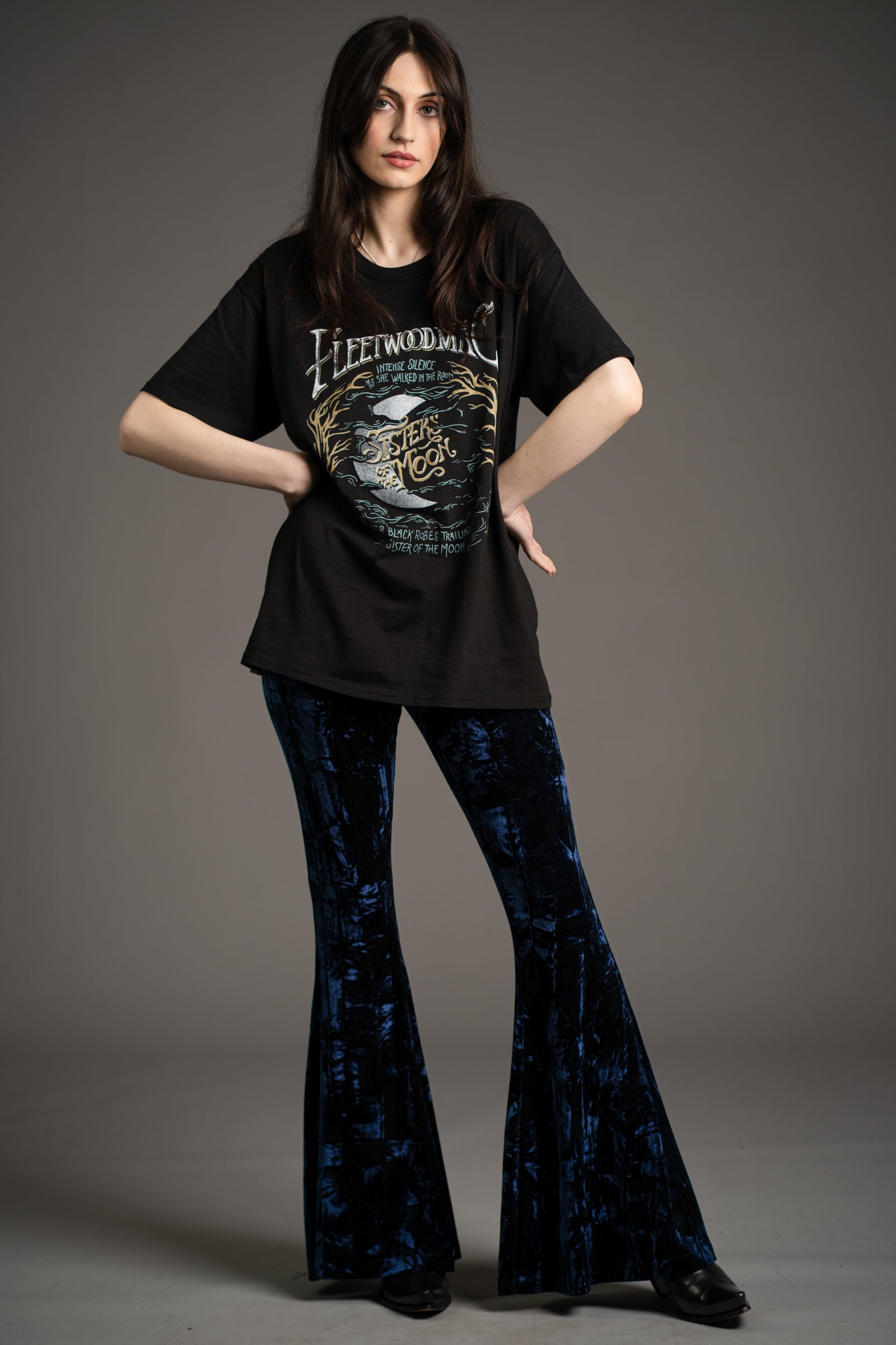 Andie models Little Lies Hendrix midnight crushed velvet flared trousers in deep blue with dramatic bell-bottom silhouette, styled with oversized Fleetwood Mac graphic tee and black ankle boots in studio setting