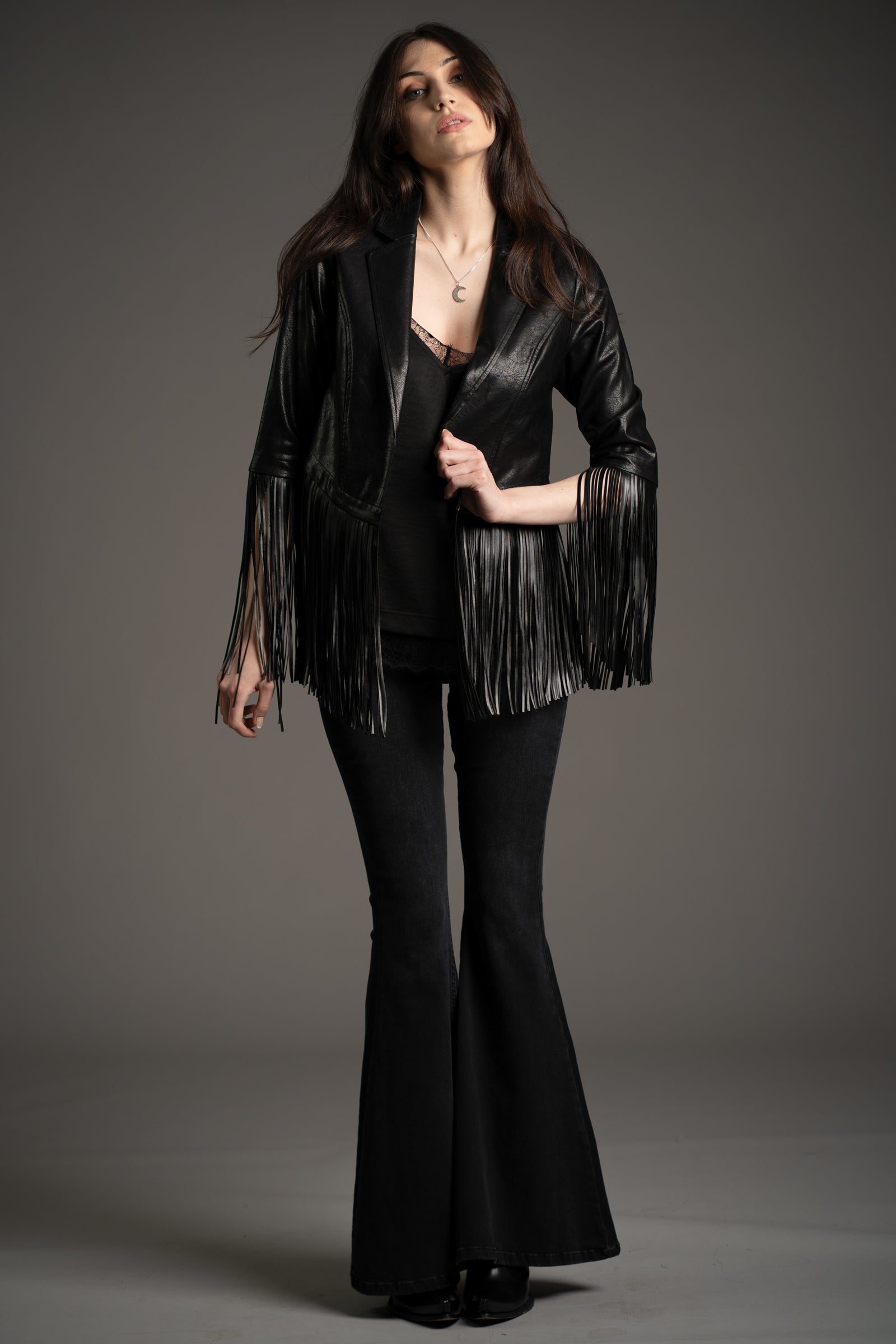Andie models Little Lies Jagger fringed faux leather jacket in black paired with denim flared trousers and cami  top