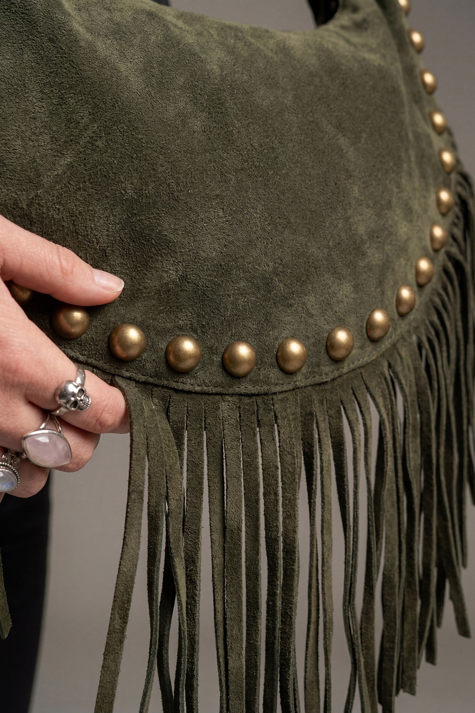 Kate Green suede handbag with gold studs and fringe held by a model.