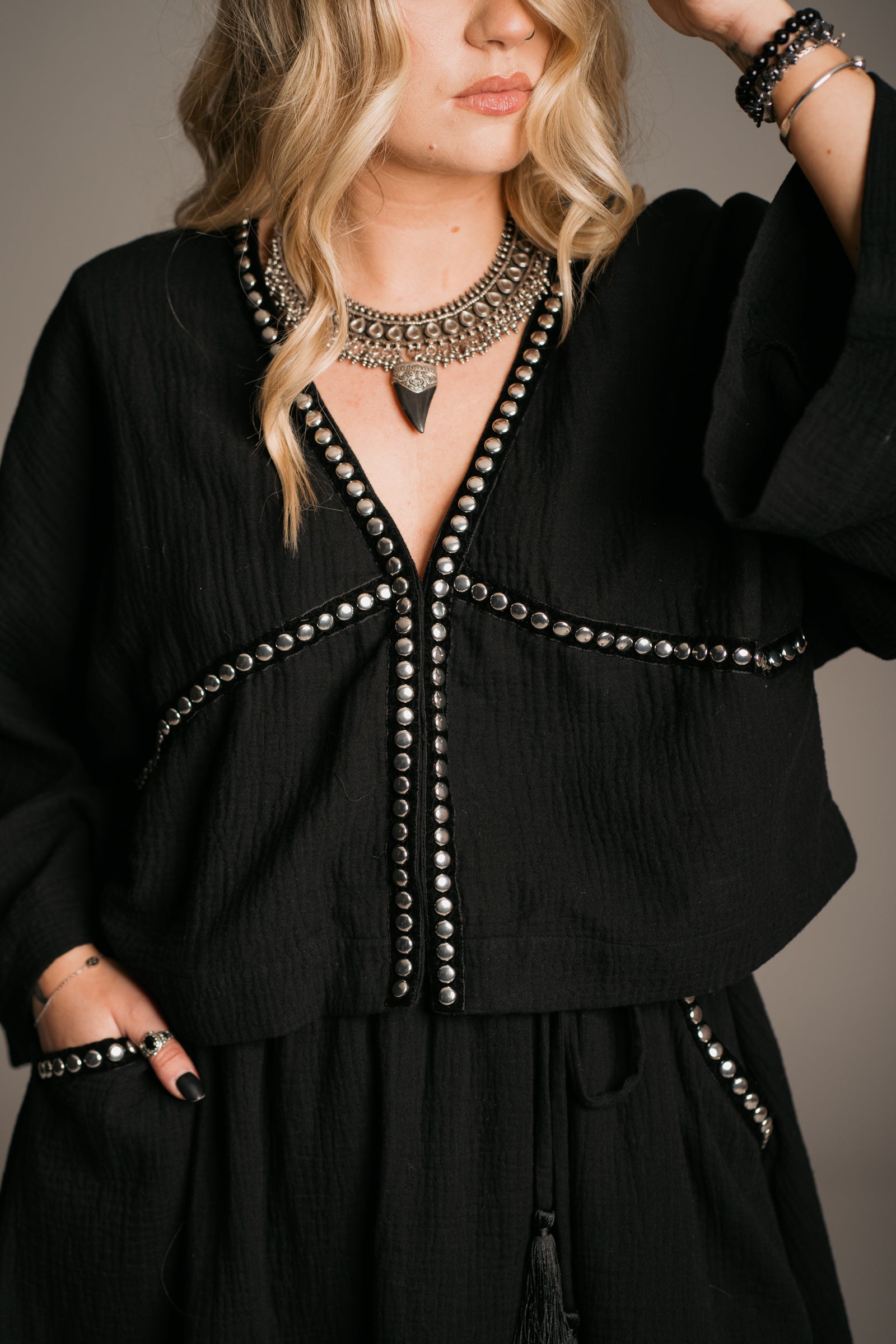 Blonde model Erin wearing the Little Lies Kravitz Black Studded Cheesecloth Co-ord, featuring silver studding along the neckline of the Kravitz Studded Top and detailed studding on the hem and pockets of the Kravitz Studded Skort. The skort is styled with a cord tie waist belt and functional pockets. Paired with a Gypsy Silver Tooth necklace, the look embodies effortless Rock 'n' Roll style