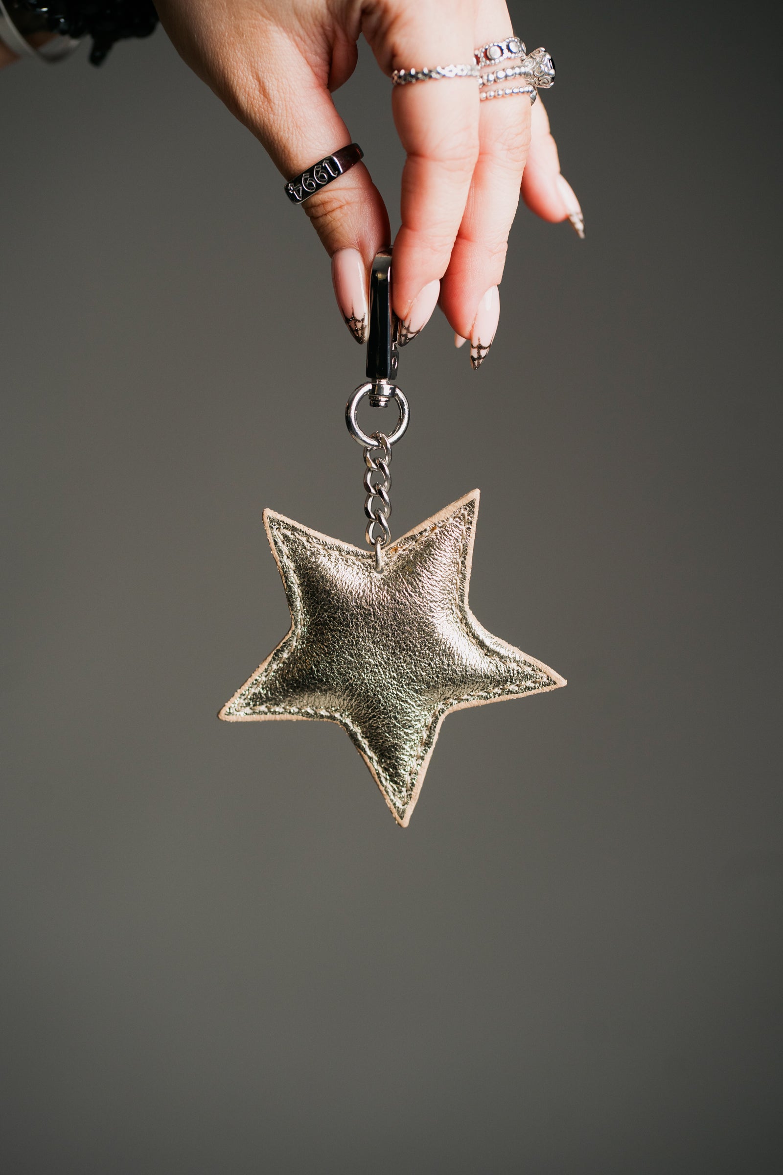 A gold genuine leather star bag charm / keyring hanging from a black strap, displayed against a patterned fabric background.