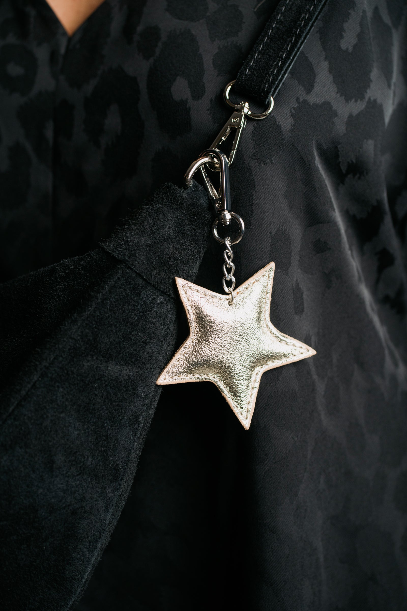 A gold genuine leather star bag charm / keyring hanging from a black strap, displayed against a patterned fabric background.