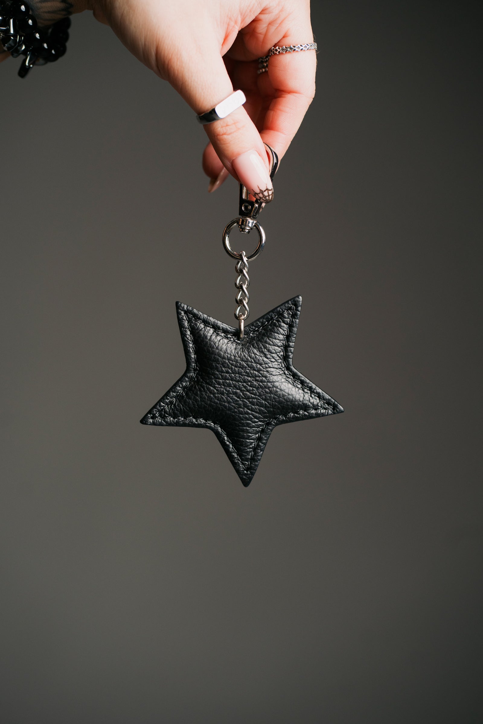 A black leather star-shaped bag charm attached to a chain, displayed against a fabric background.