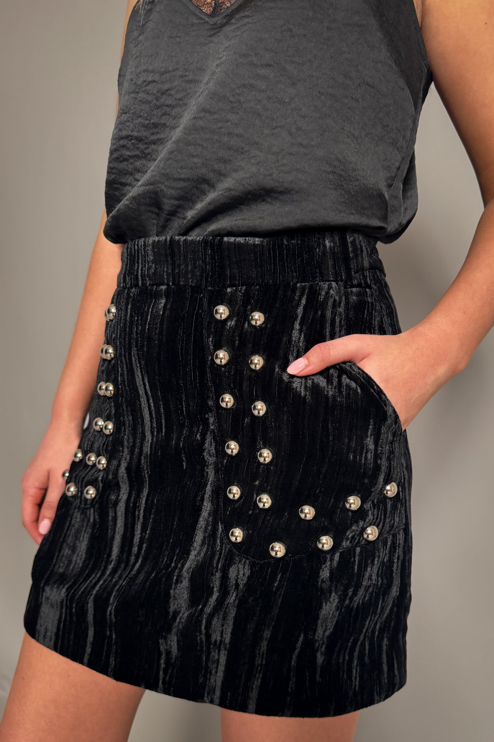 Close-up of Little Lies Lennon velvet mini skirt showing soft black textured fabric and silver stud embellishment on front pockets