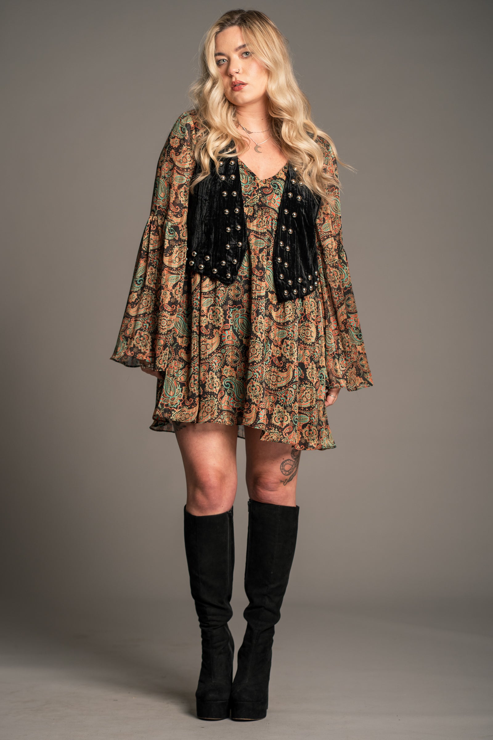 Model wearing Little Lies Lennon black studded velvet waistcoat styled with printed boho mini dress and knee-high boots for relaxed everyday outfit